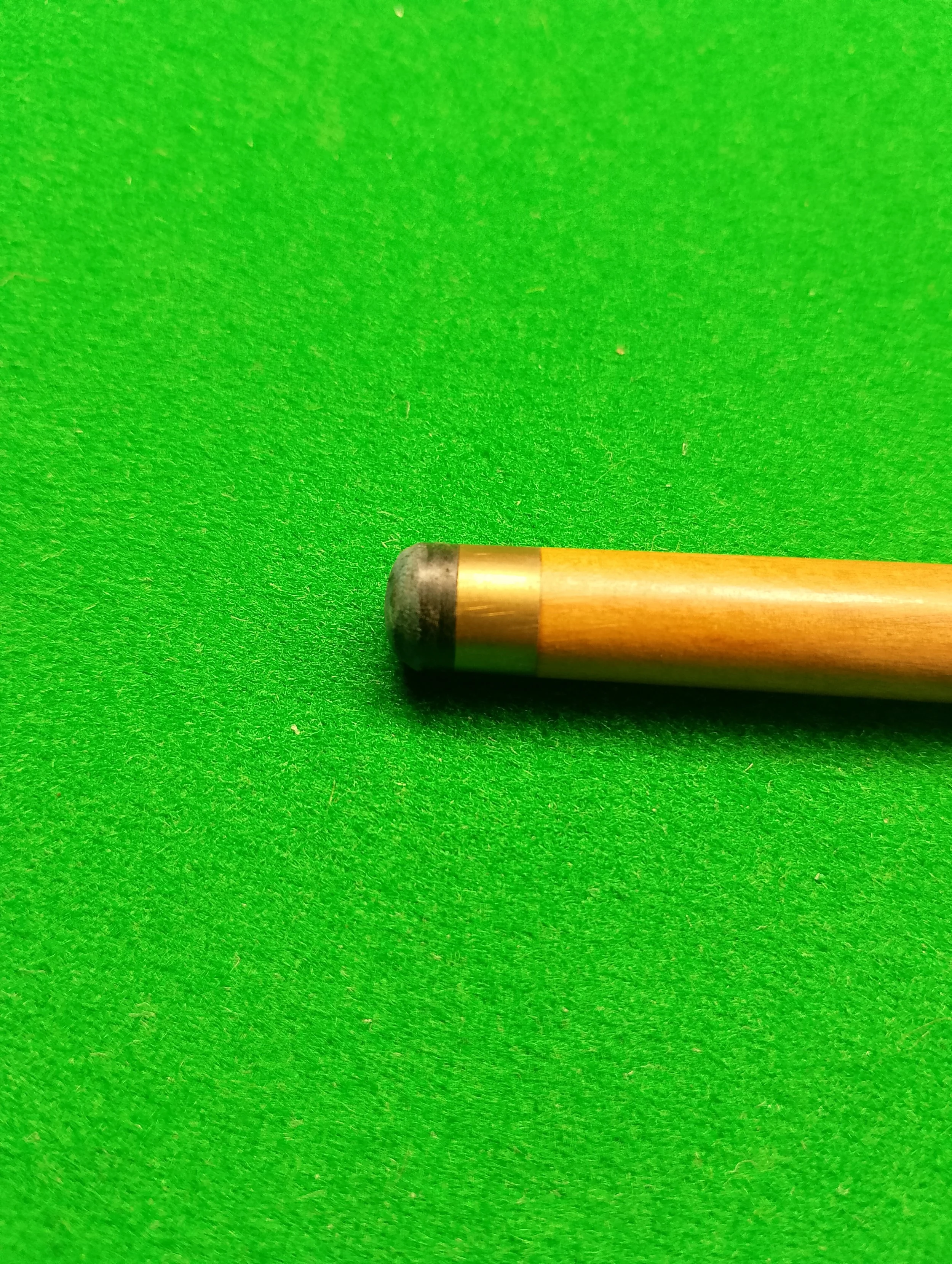 A cue stick for billiards or pool resting on a green felt table.