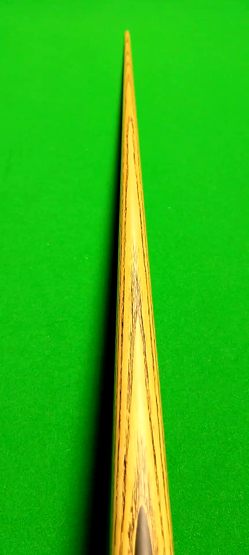 Close-up of a wooden cue stick on a green billiard or pool table.