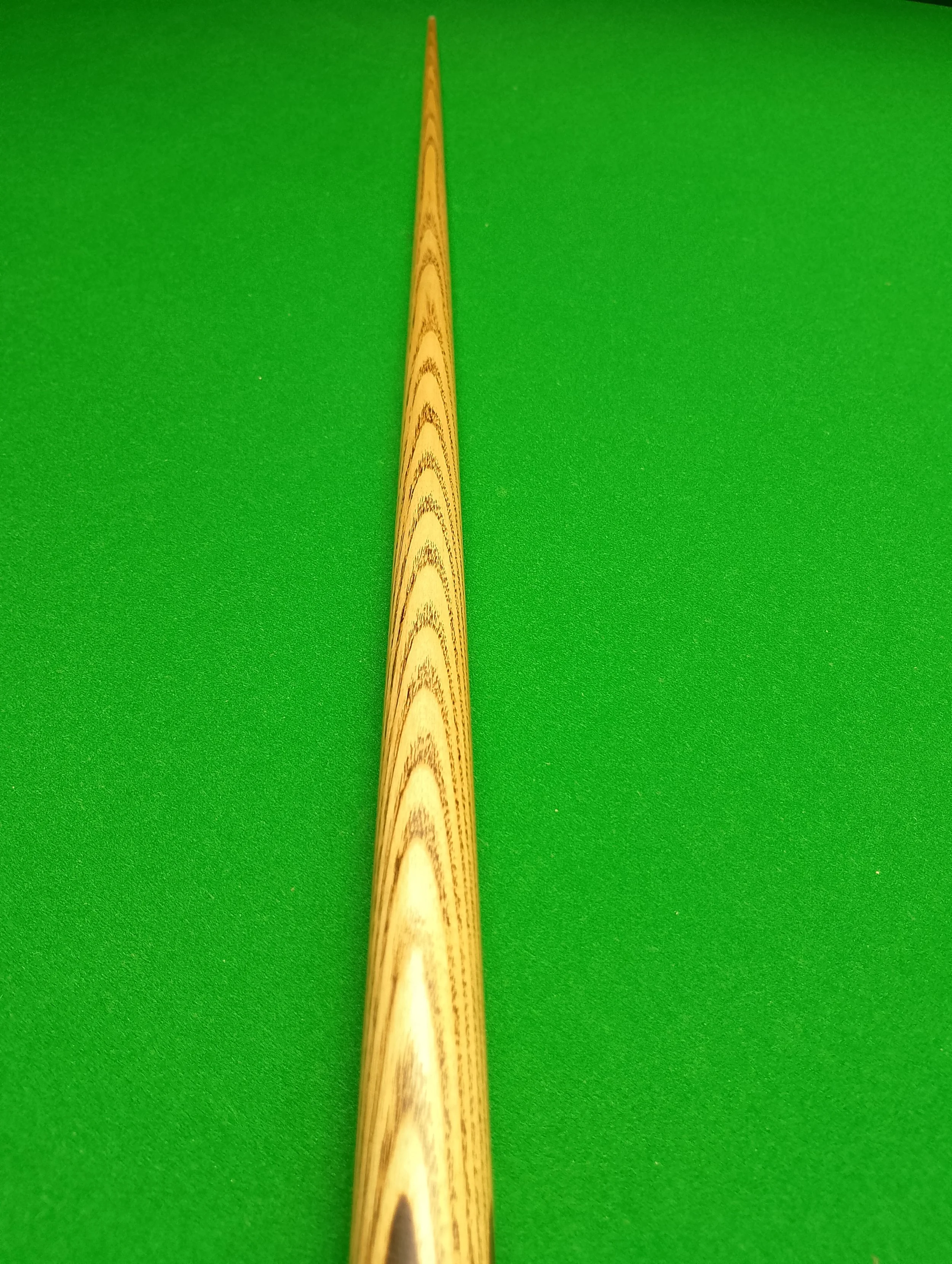 An angled view of a wooden cue stick on a green pool or billiards table.