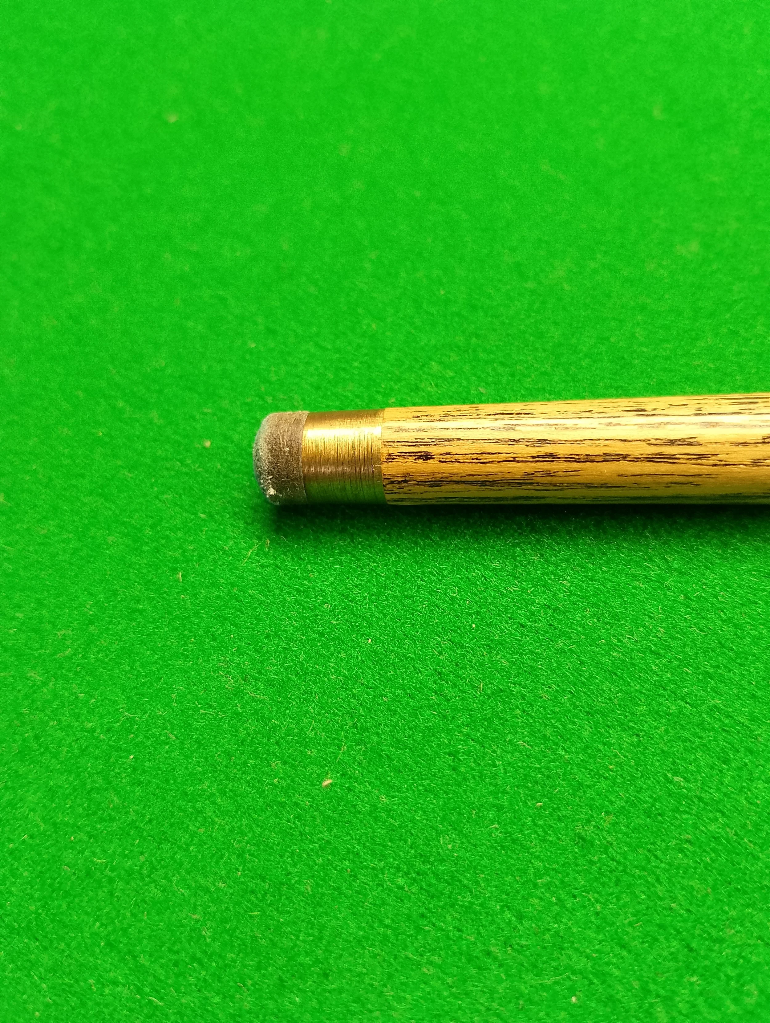 Close-up of a cue stick tip resting on a green felt surface.