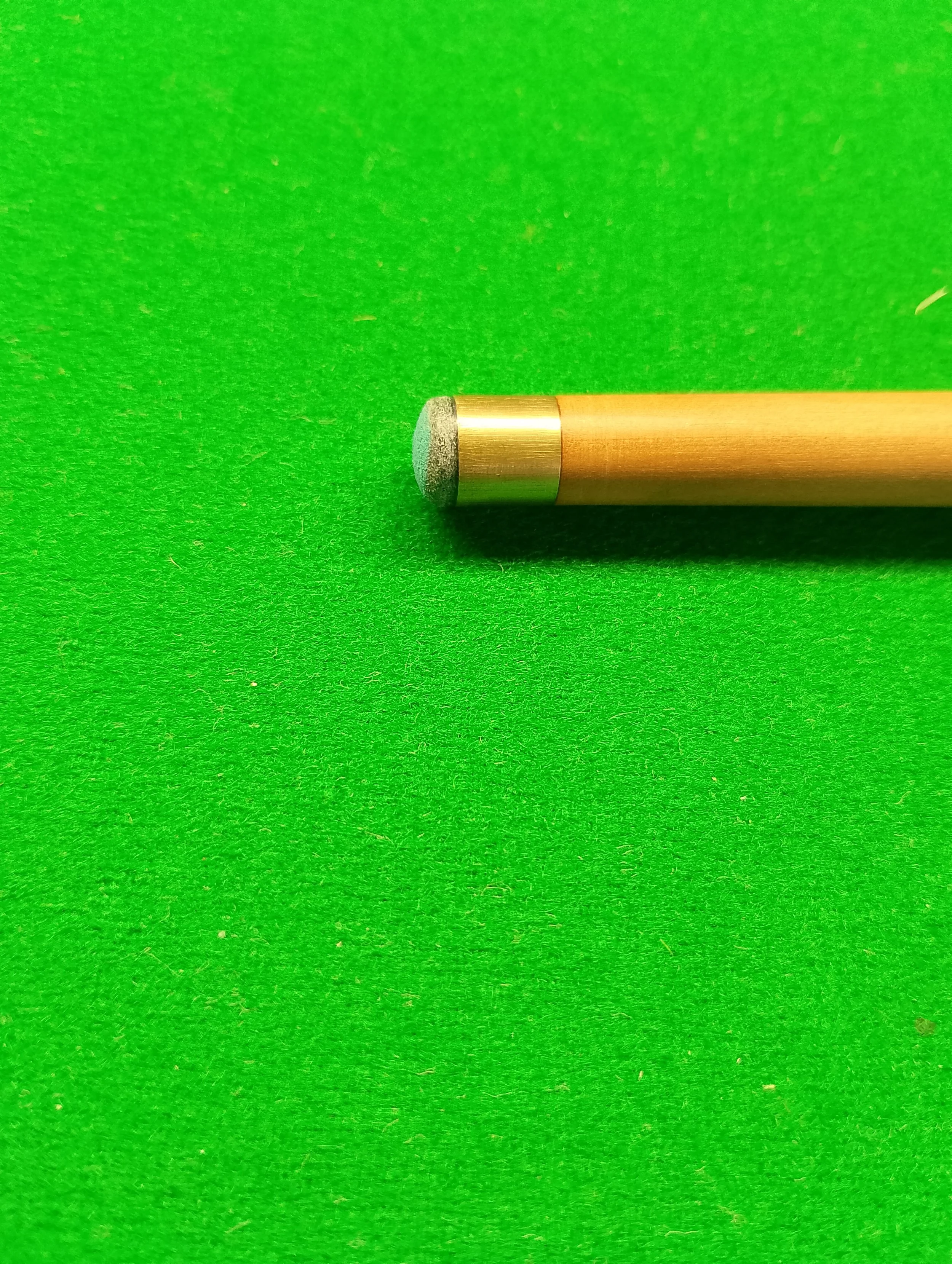 A cue stick with a black chalk tip lying on a green billiards or pool table.