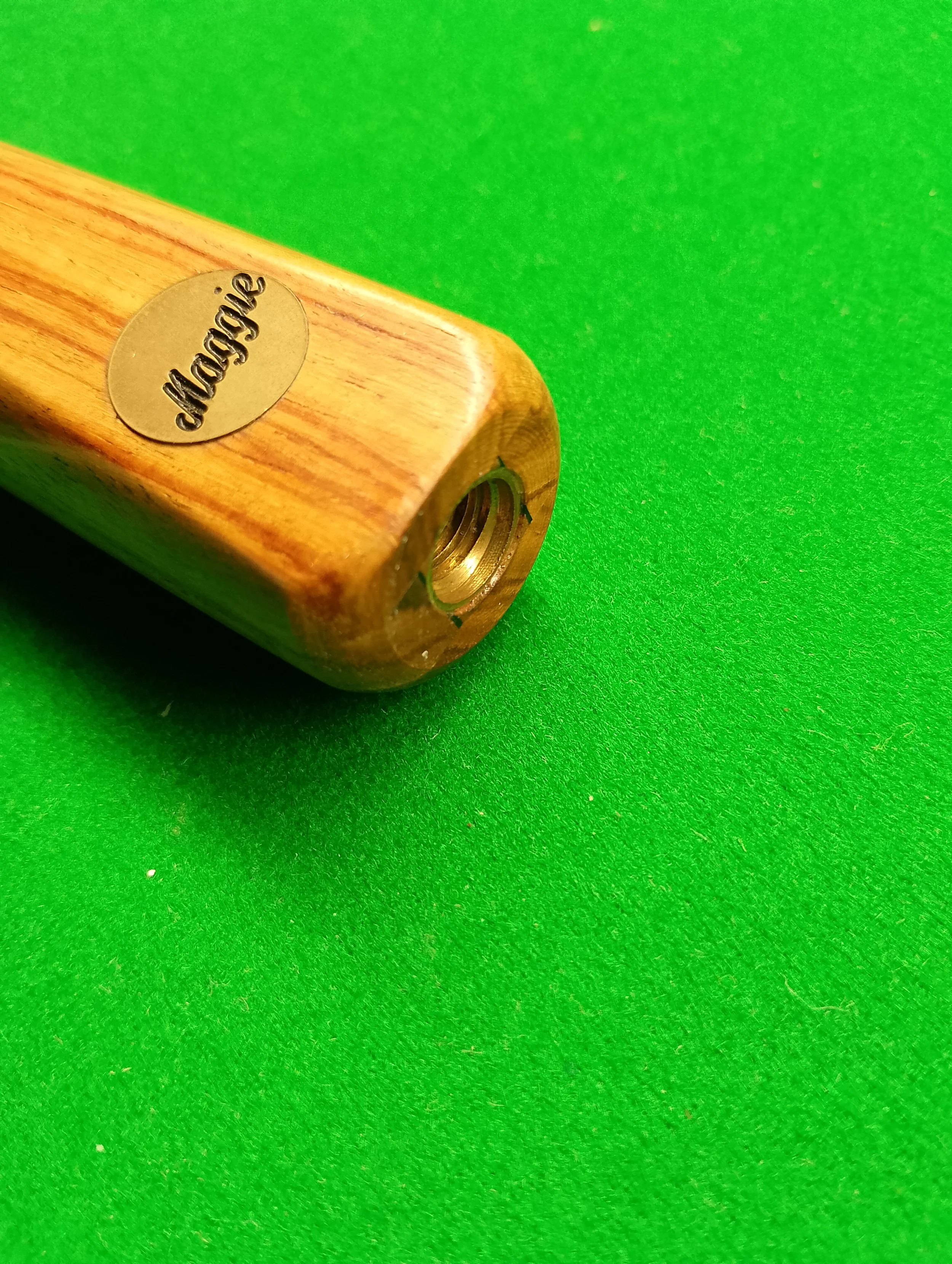 Close-up of a wooden object with a metal insert and a Goldie logo on a bright green surface.