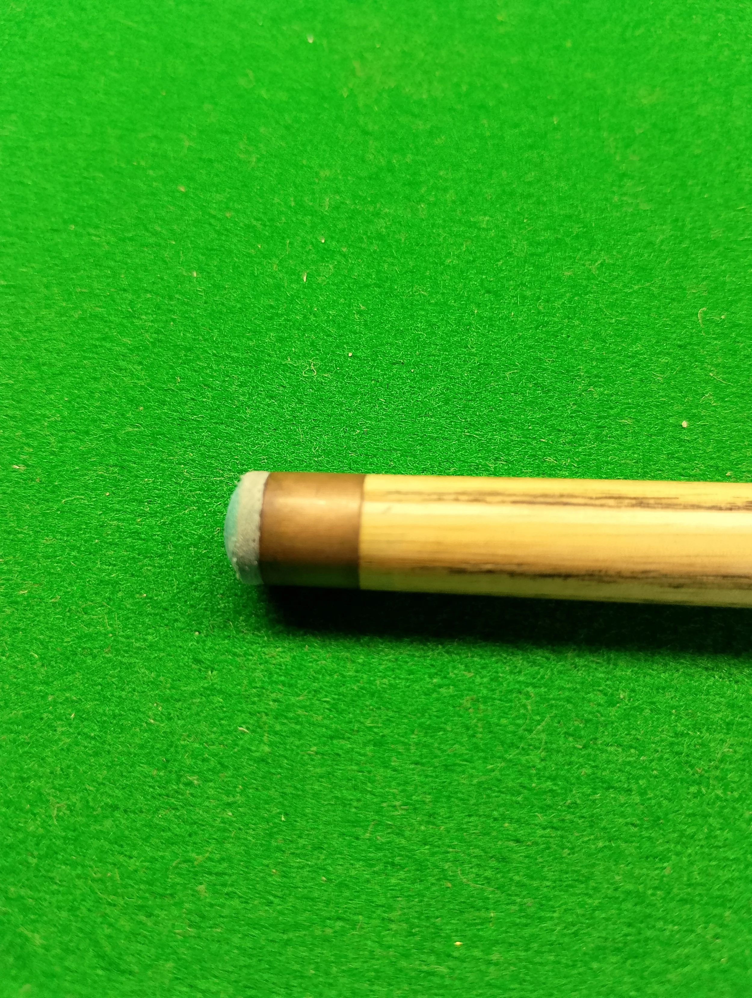Close-up of a pool cue stick on a green pool table.
