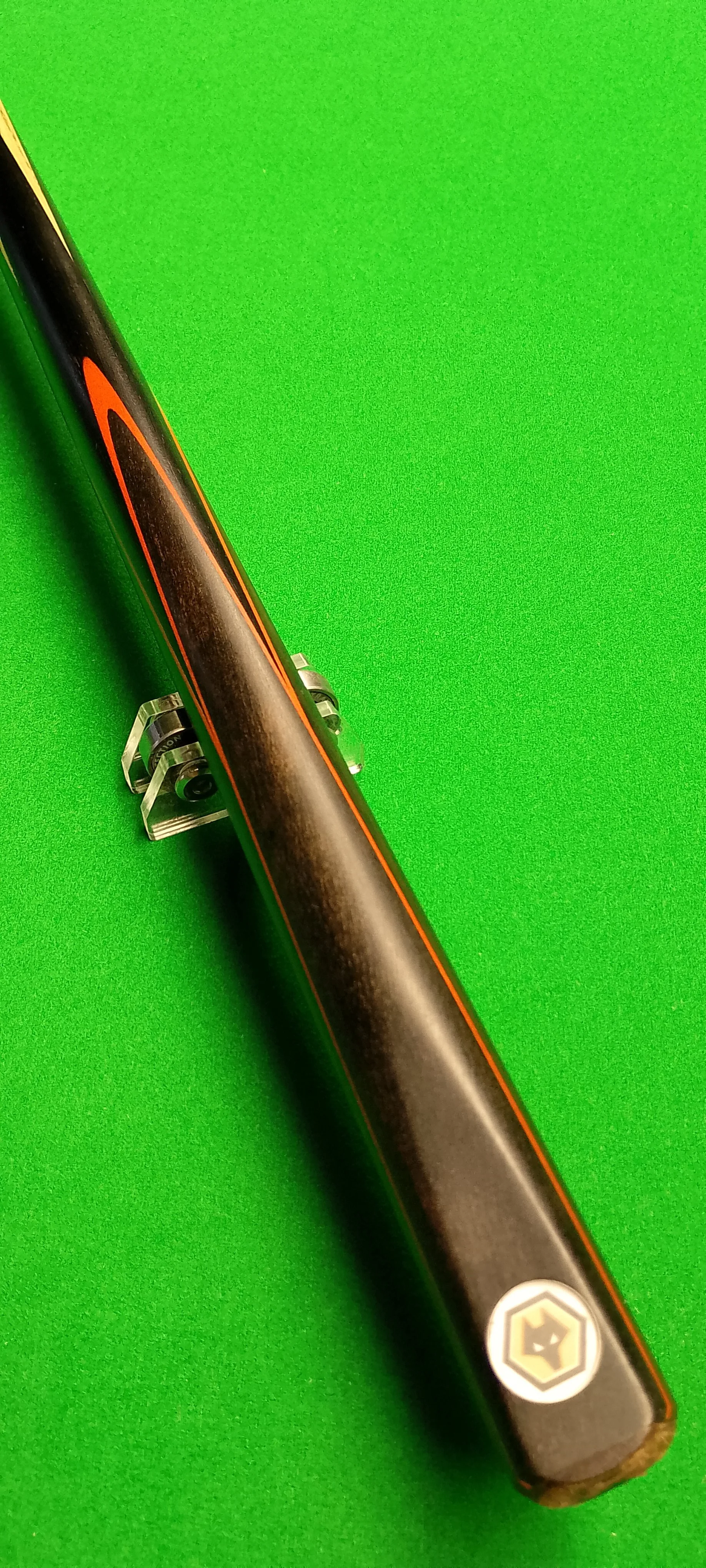Close-up of a black and orange pool cue stick resting on a clear cue holder on a bright green pool table.