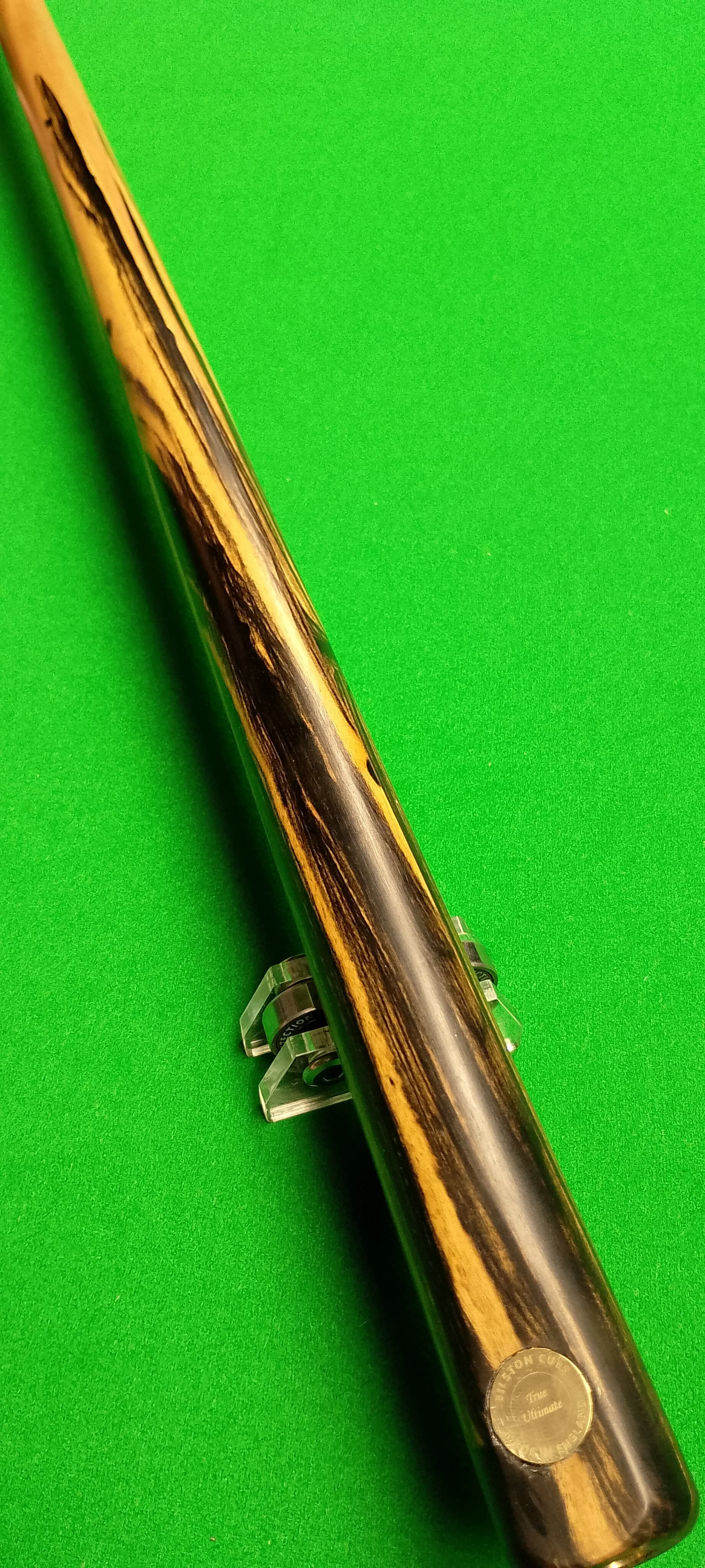 Close-up of a pool cue with a black and tan wood grain pattern, resting on a green billiard table.