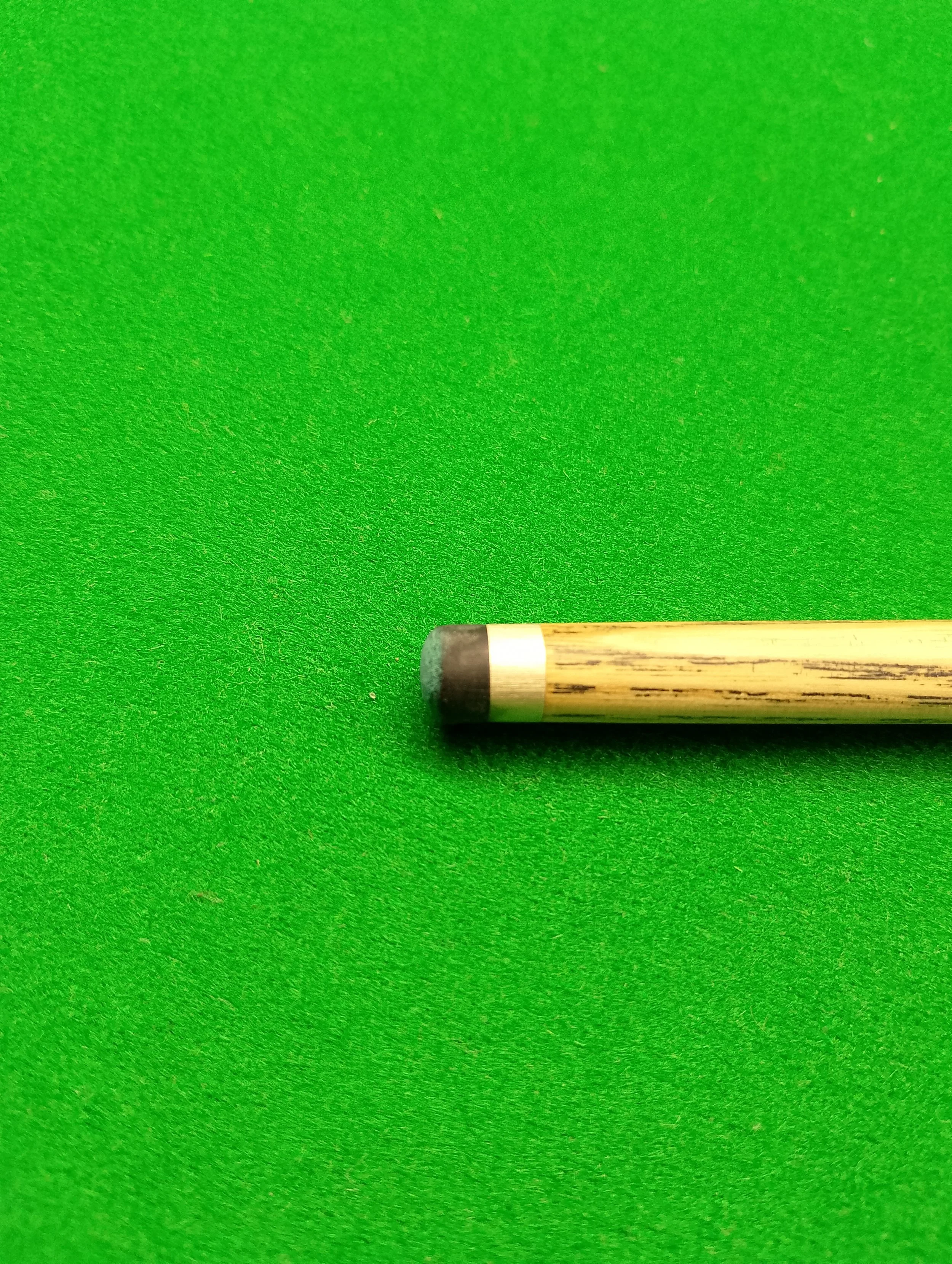 Close-up of a pool cue stick resting on green felt.