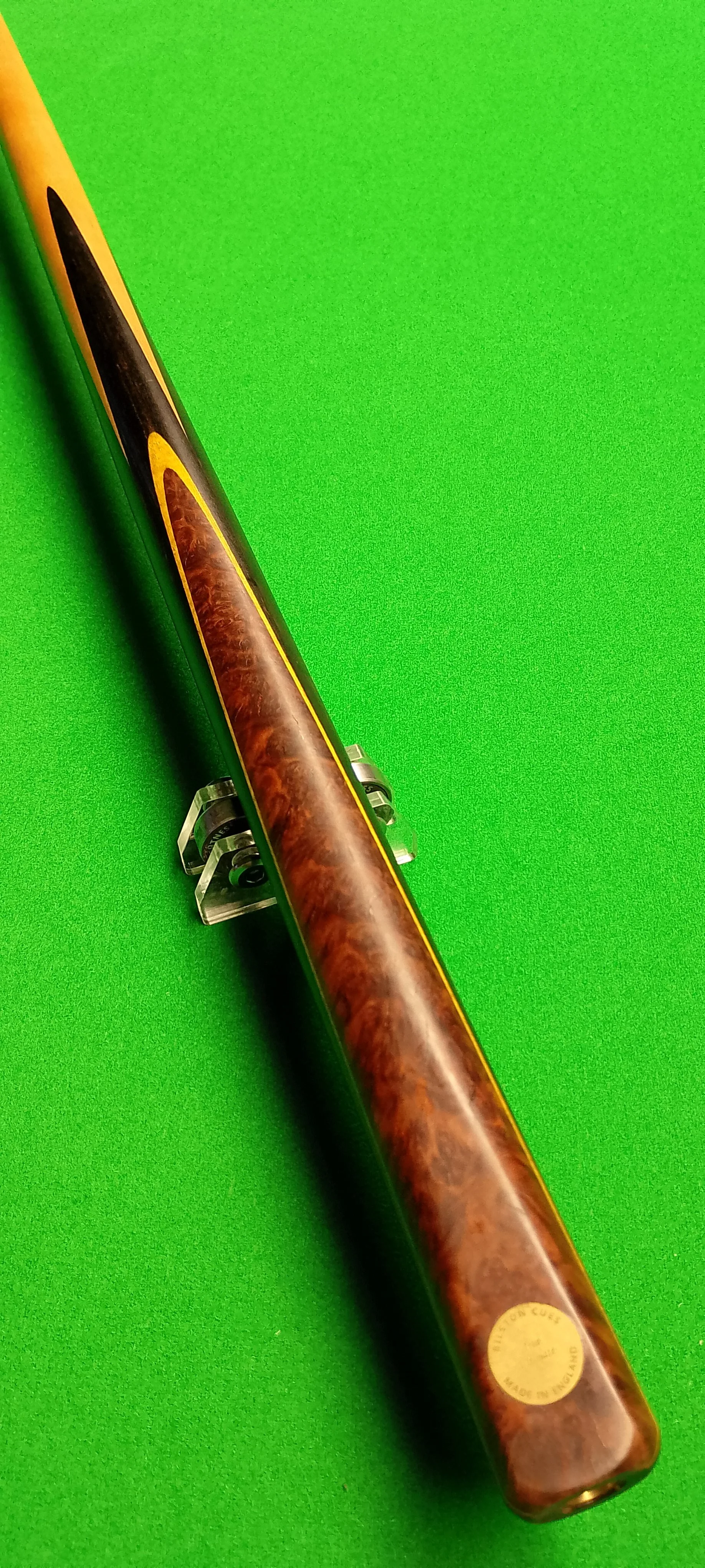 Close-up of a cue stick with a brown wood grain pattern, placed on a green pool table surface.