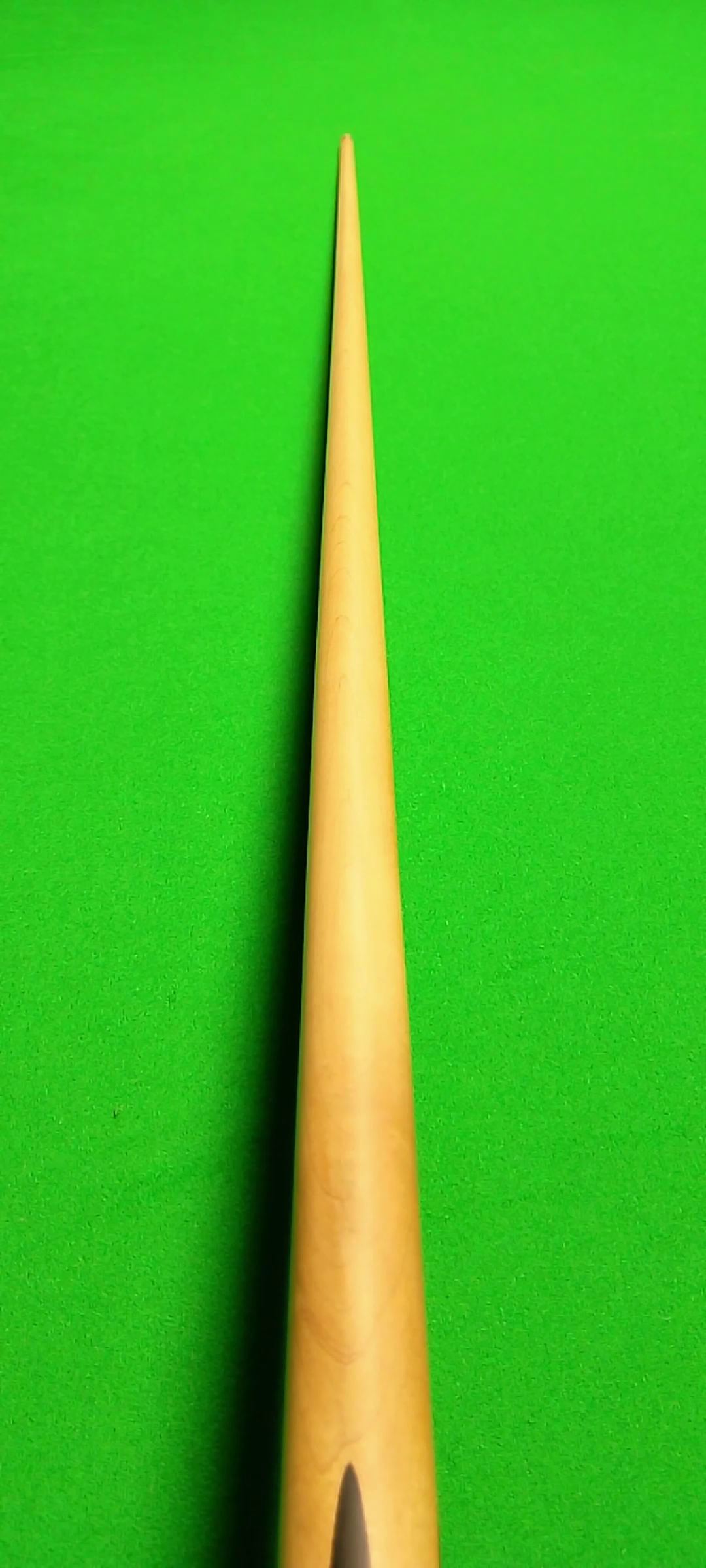Close-up of a yellow cue stick on a bright green pool table felt.