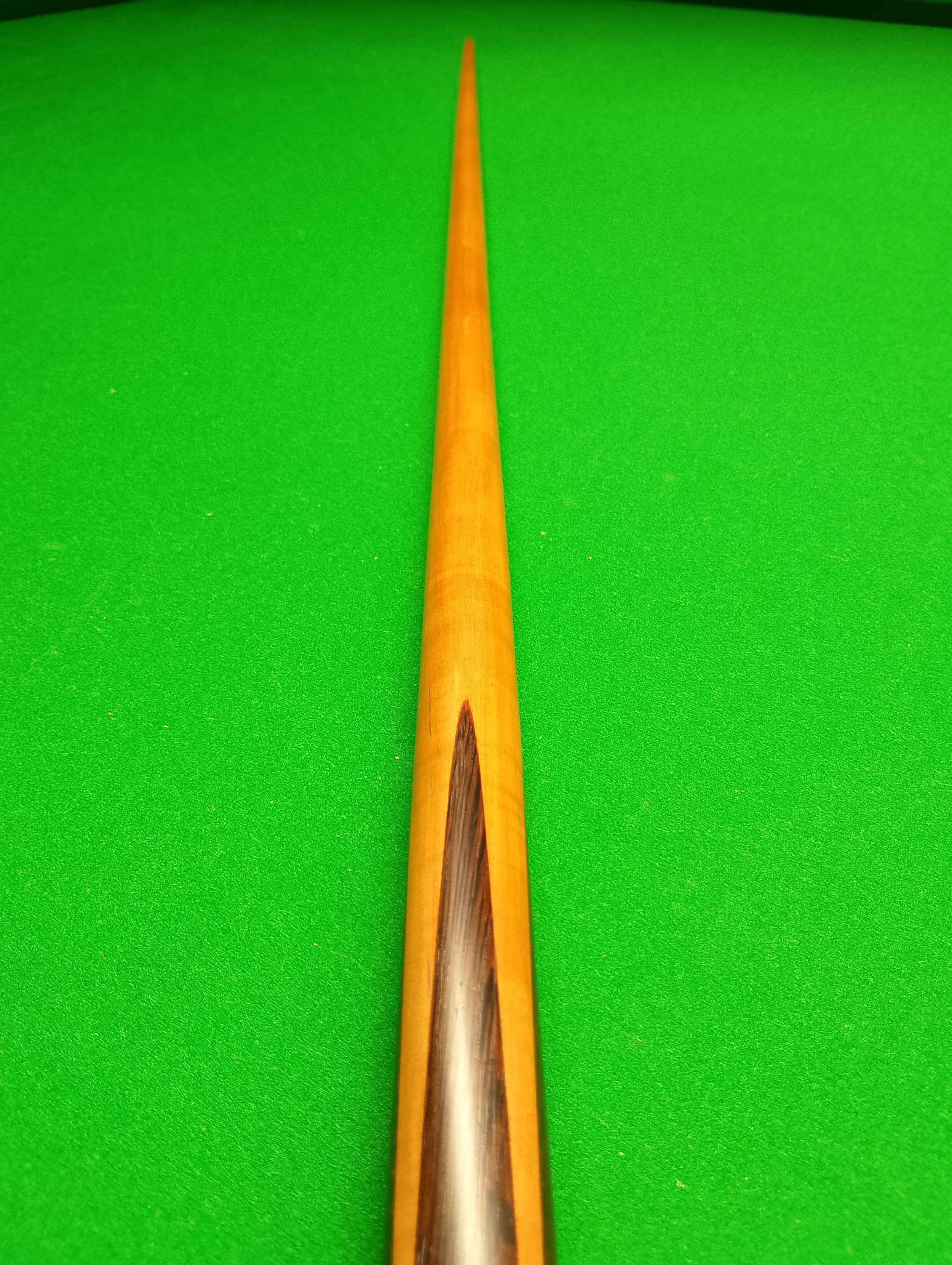 Close-up view of a snooker cue stick on a green snooker table.