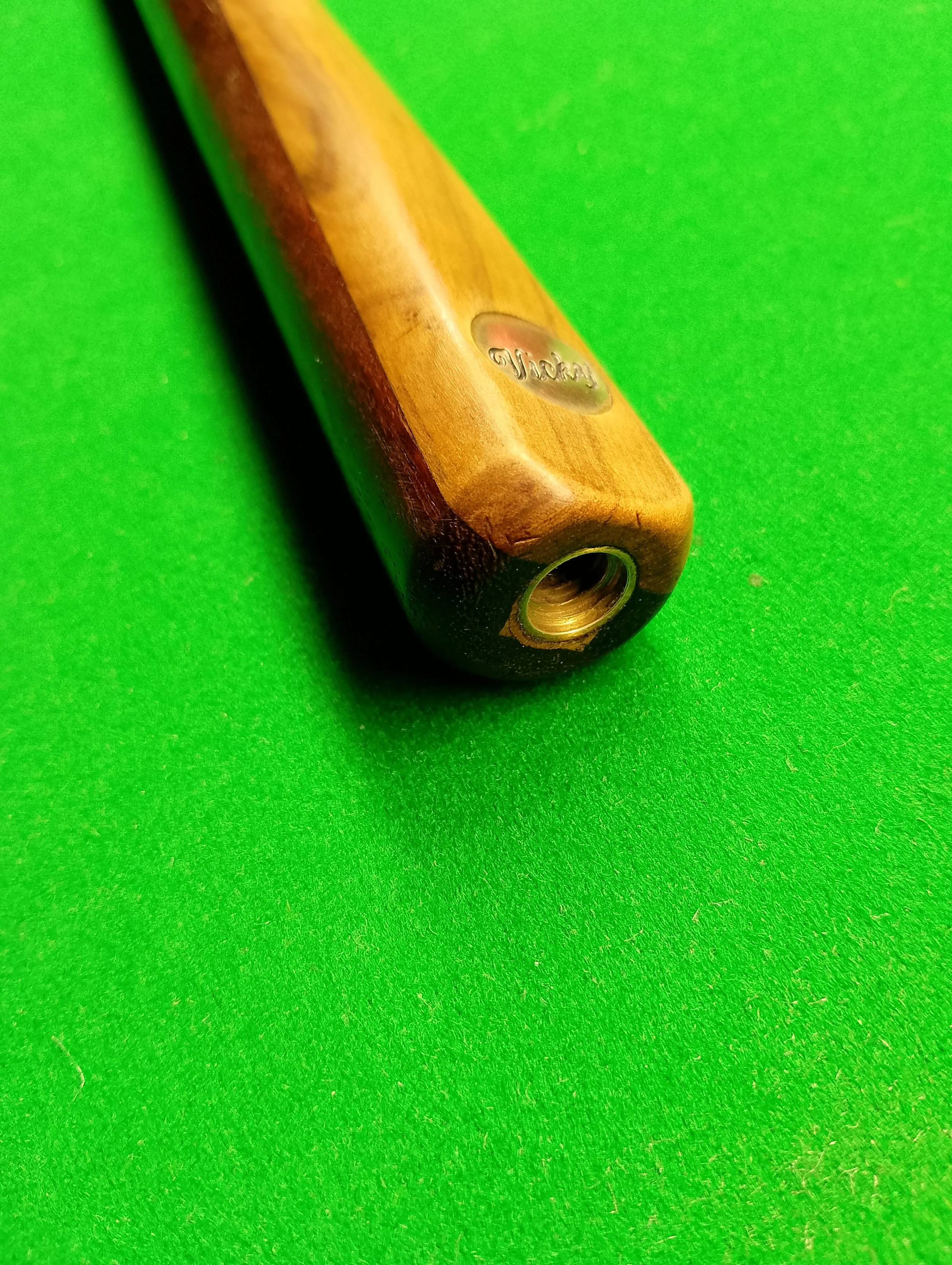 Close-up of the butt end of a wooden pool cue stick on a green pool table felt.