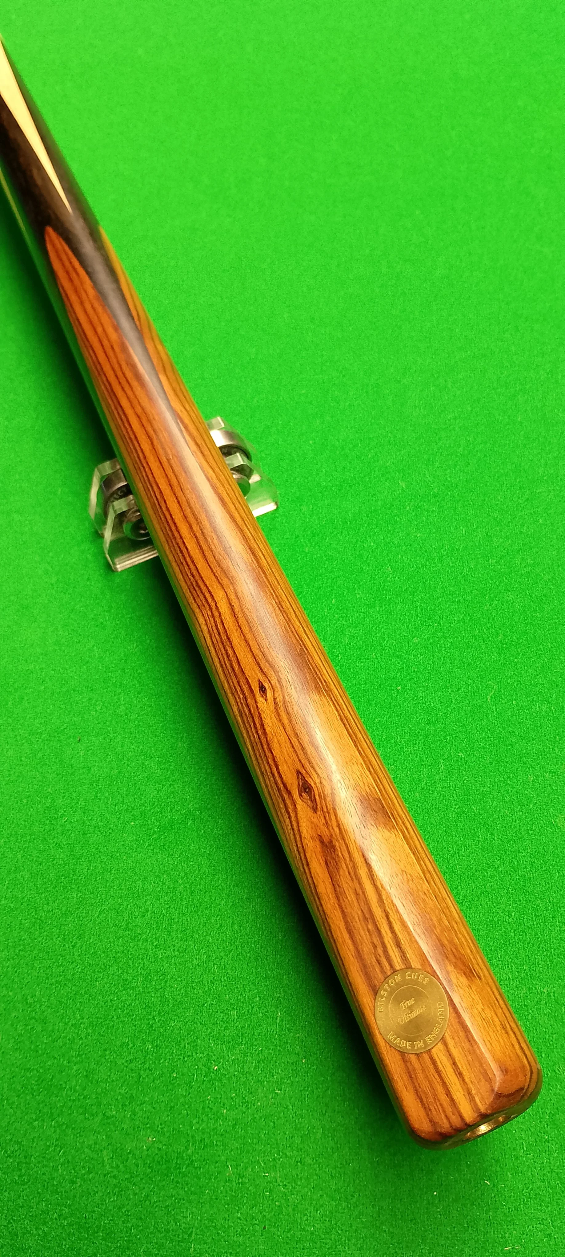 A shot of a cue stick for playing billiards or pool with a wooden handle and engraved label, lying on a green pool table felt.