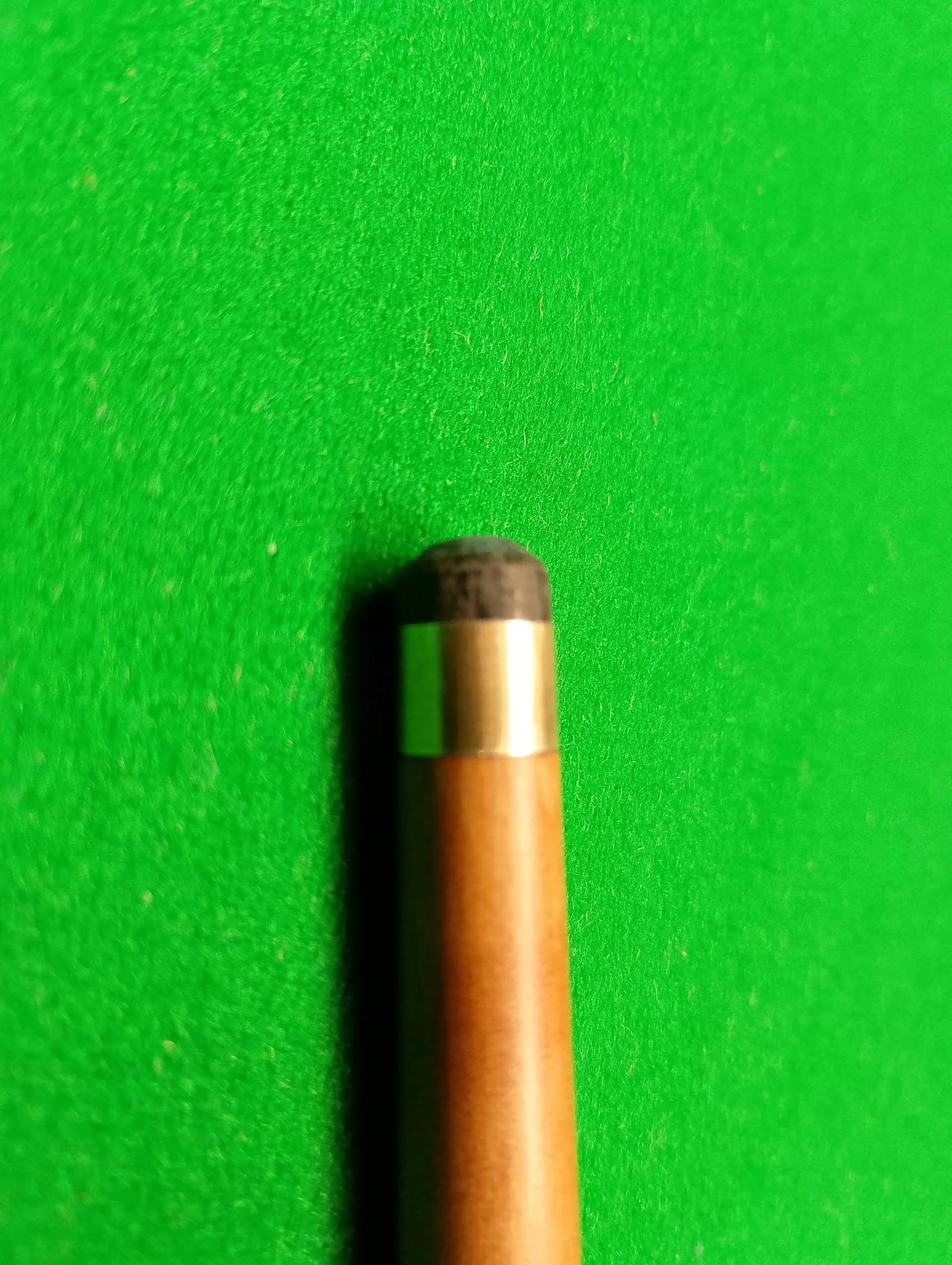Close-up of the tip of a wooden pencil with a black eraser on a bright green textured surface.