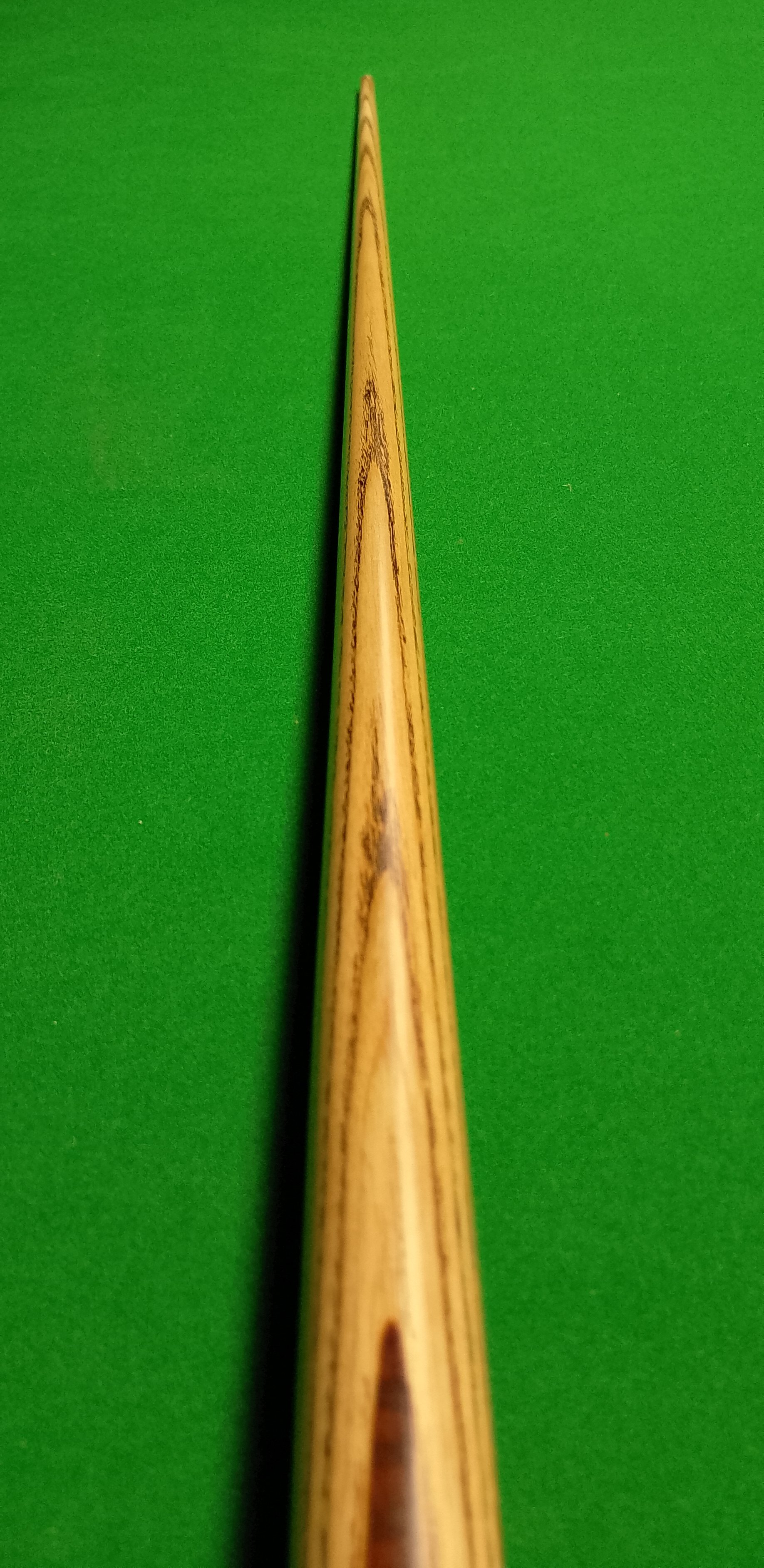 Close-up of a wooden cue stick on a green billiards or pool table.