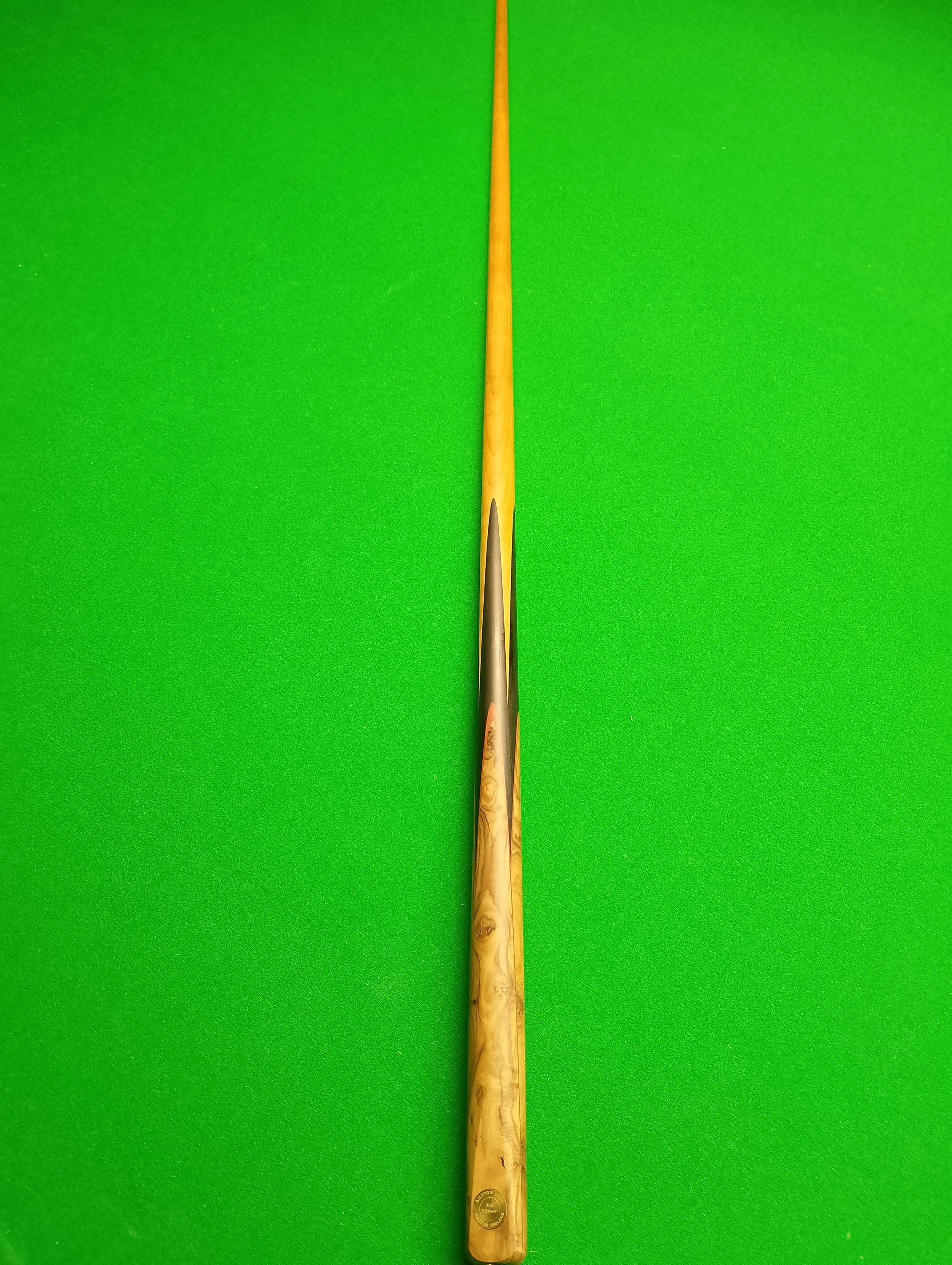 A close-up of a pool cue stick lying on a green pool table.