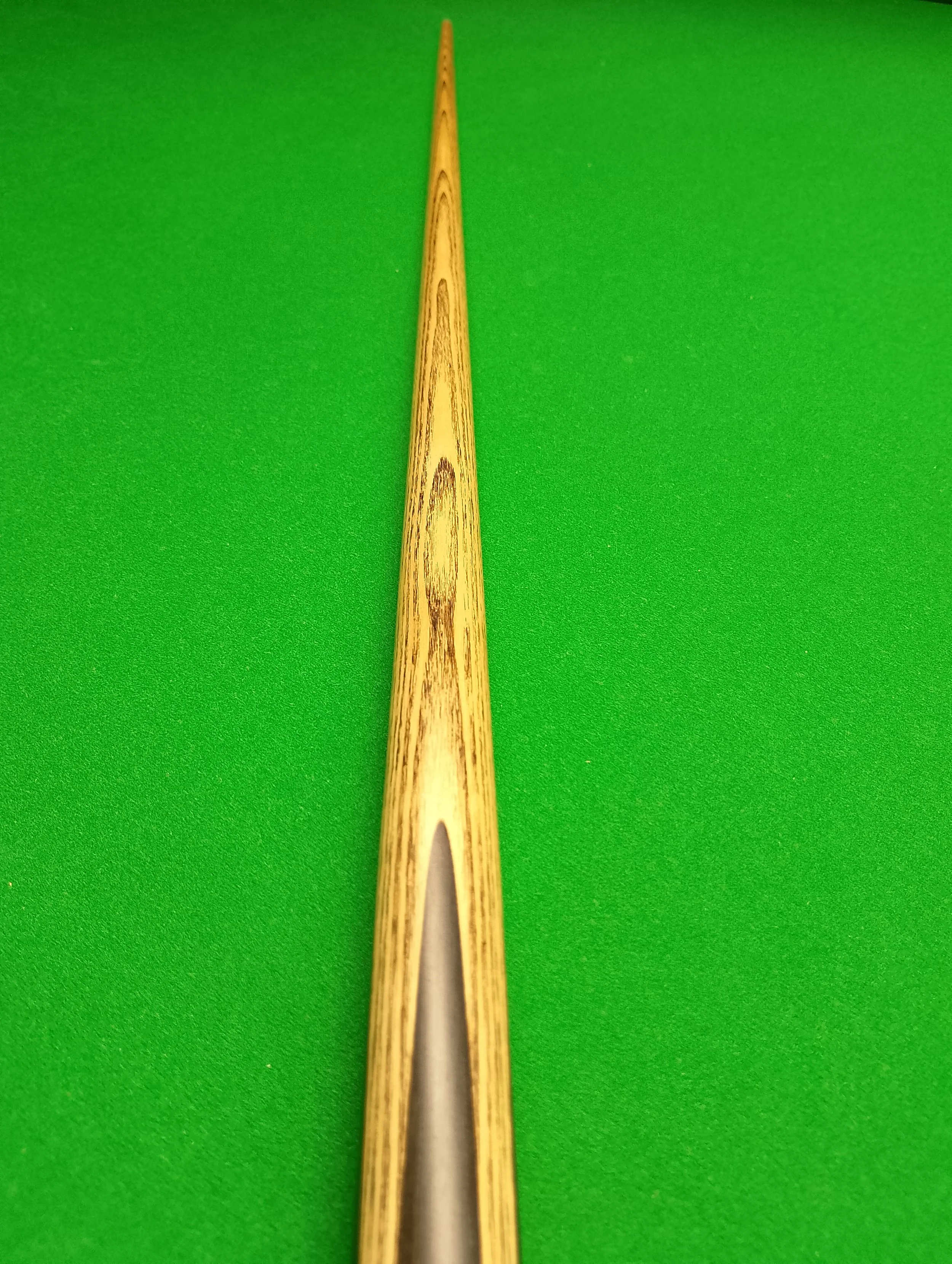 A wooden cue stick used for playing pool or billiards, placed vertically on a green felt table.