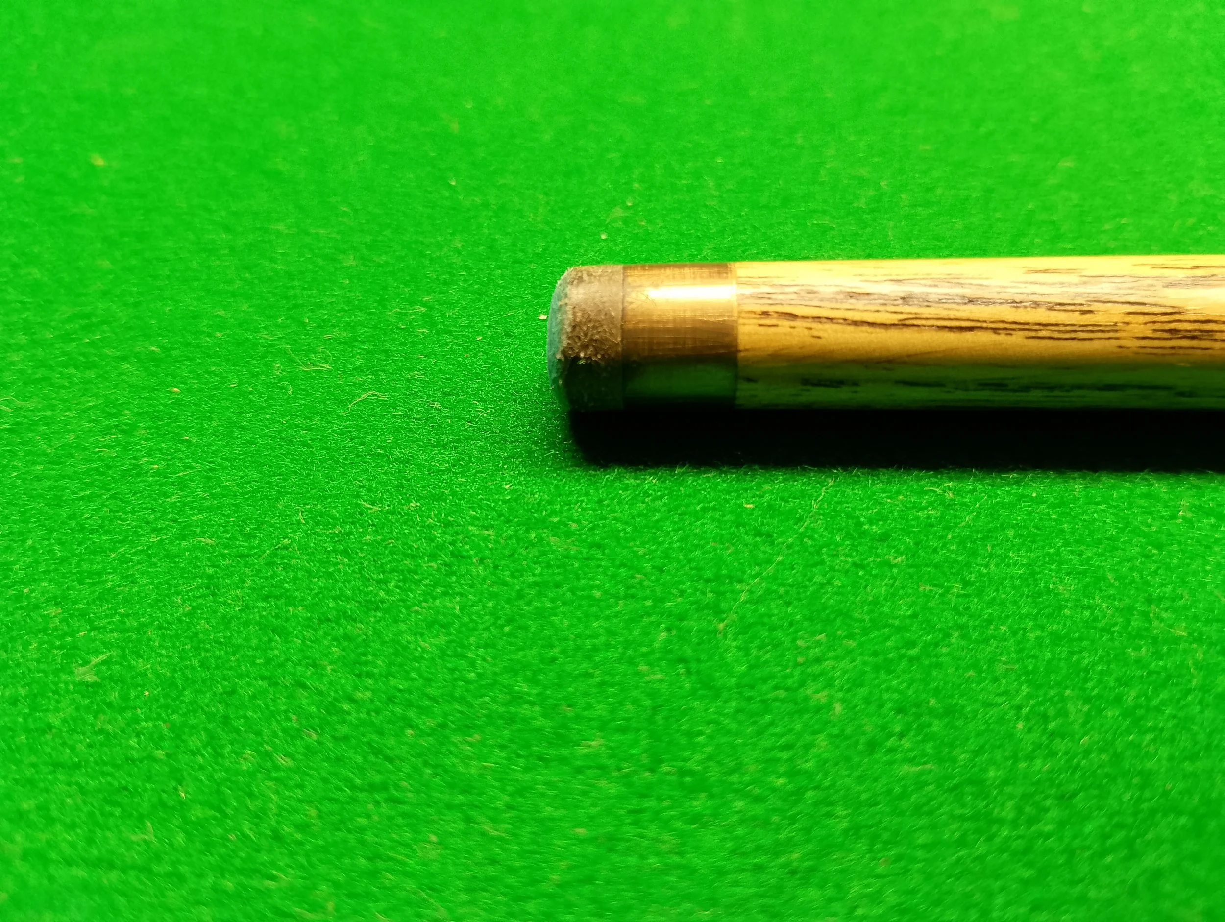 Close-up of a wooden pool cue stick on a green pool table.
