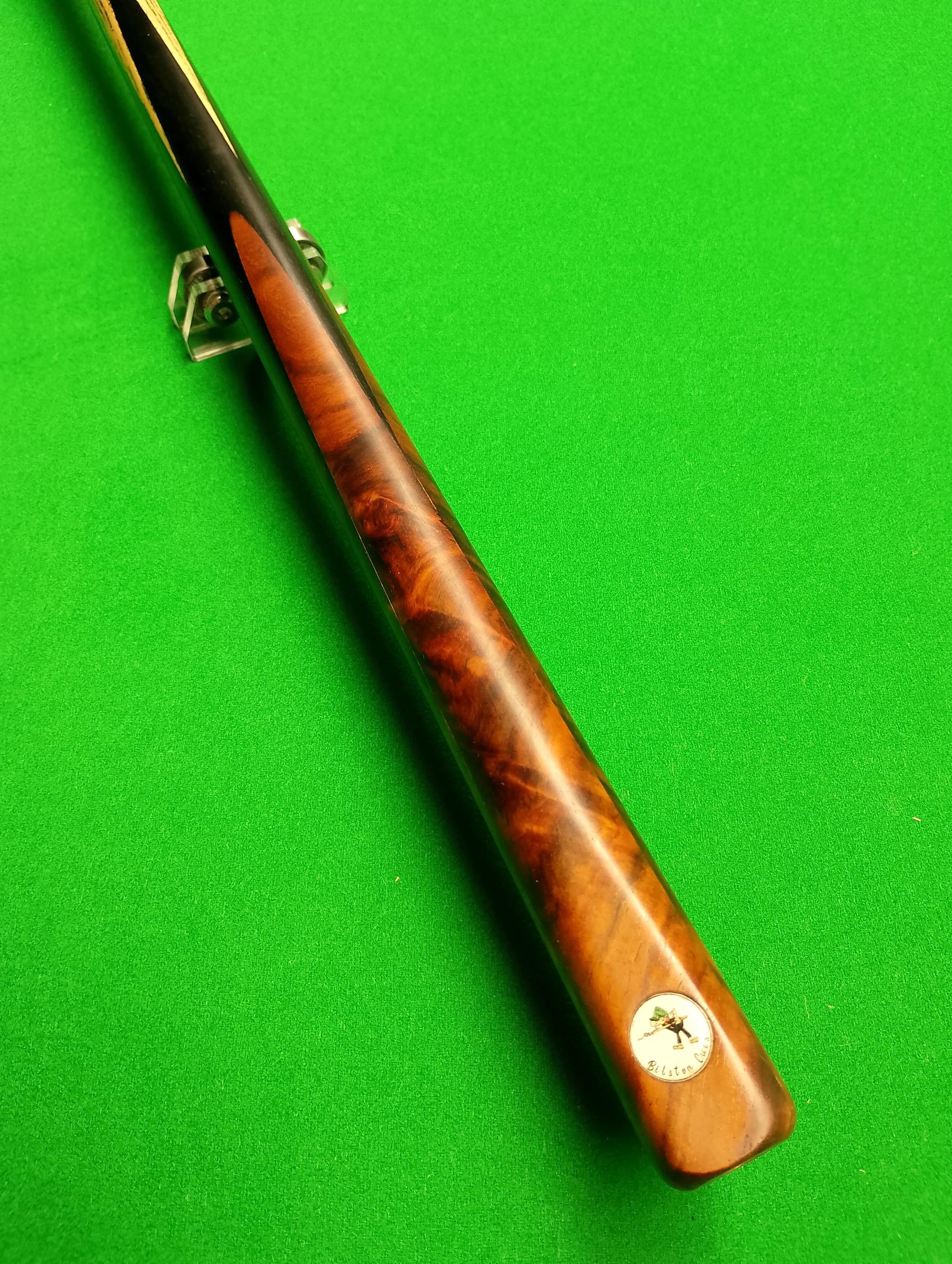 A billiard cue stick with a wooden finish and metal hardware, resting on a green billiard table surface.