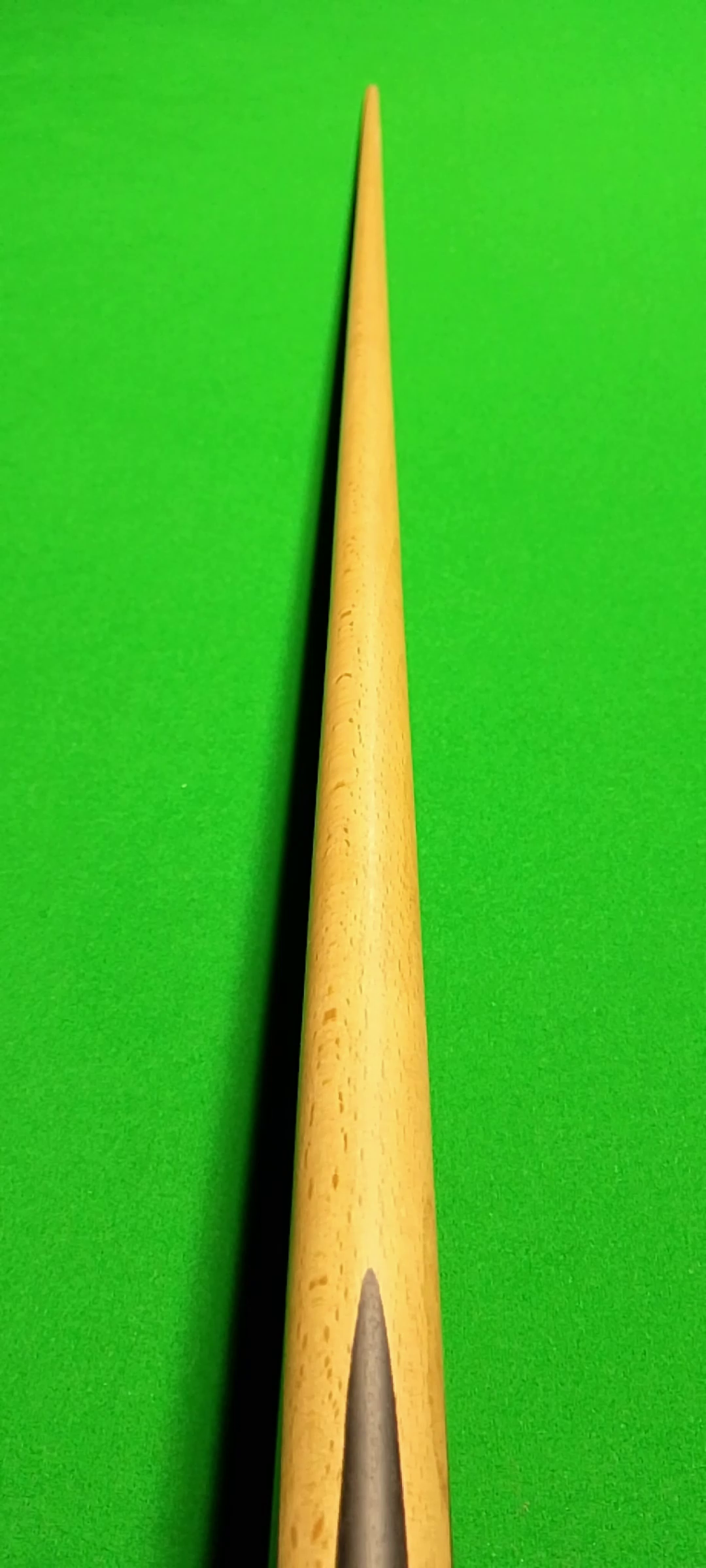 A close-up shot of a wooden cue stick placed on a green billiard or pool table.