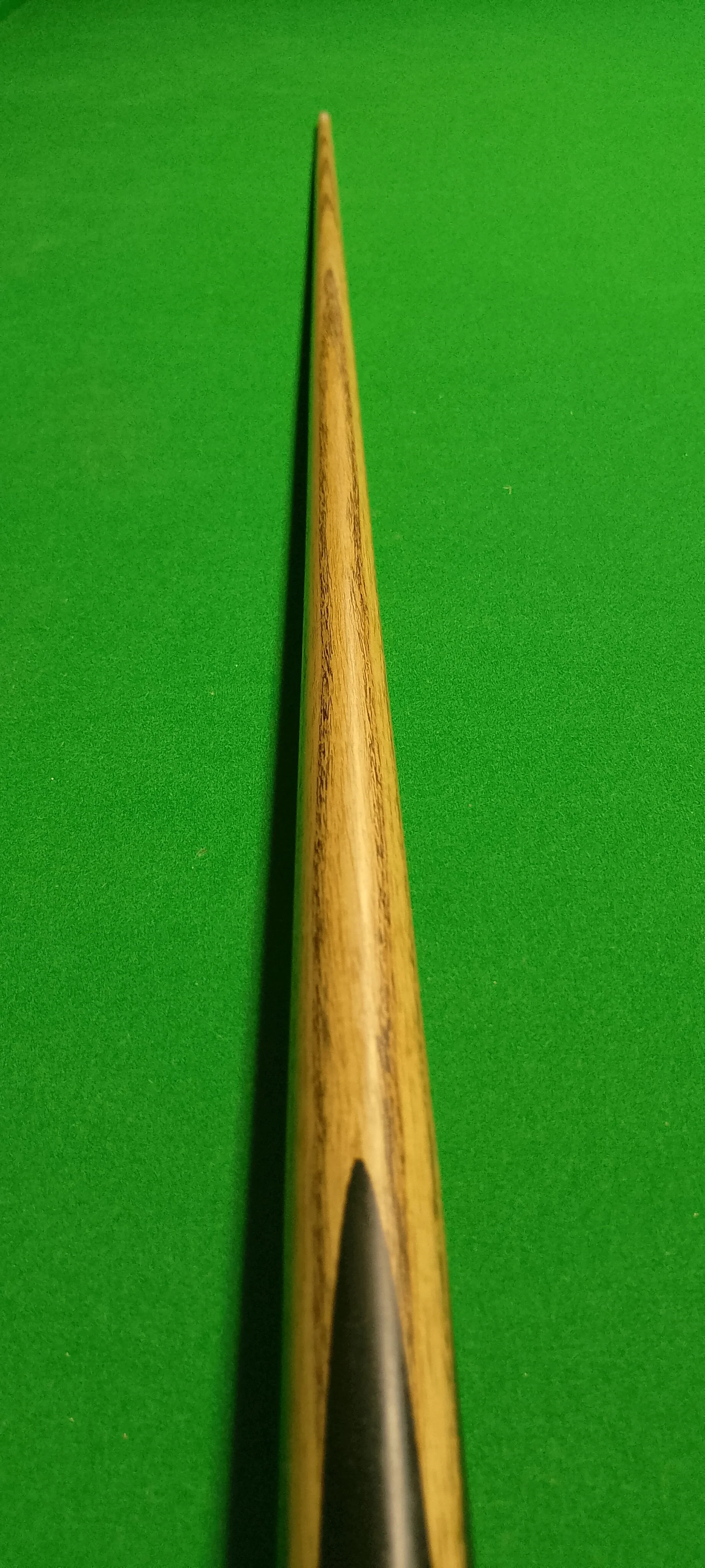 Close-up of the tip of a wooden cue stick against a green pool or snooker table surface.