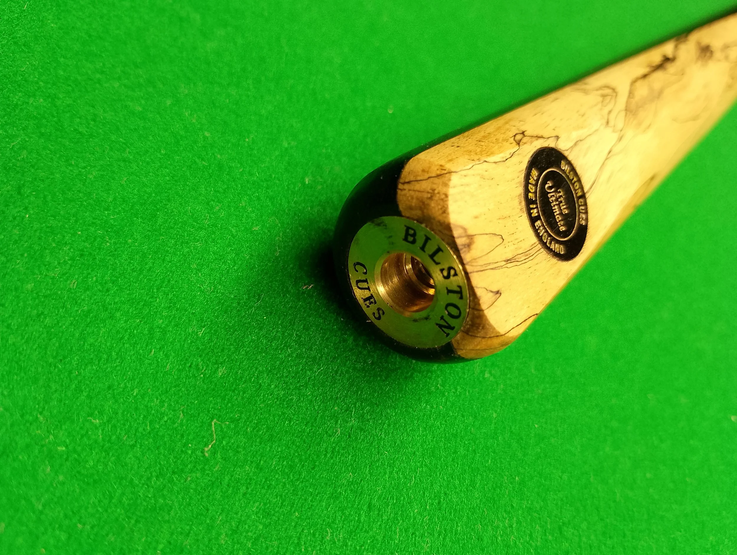 Top view of a cue stick with a black and wooden design, resting on a green pool table surface.