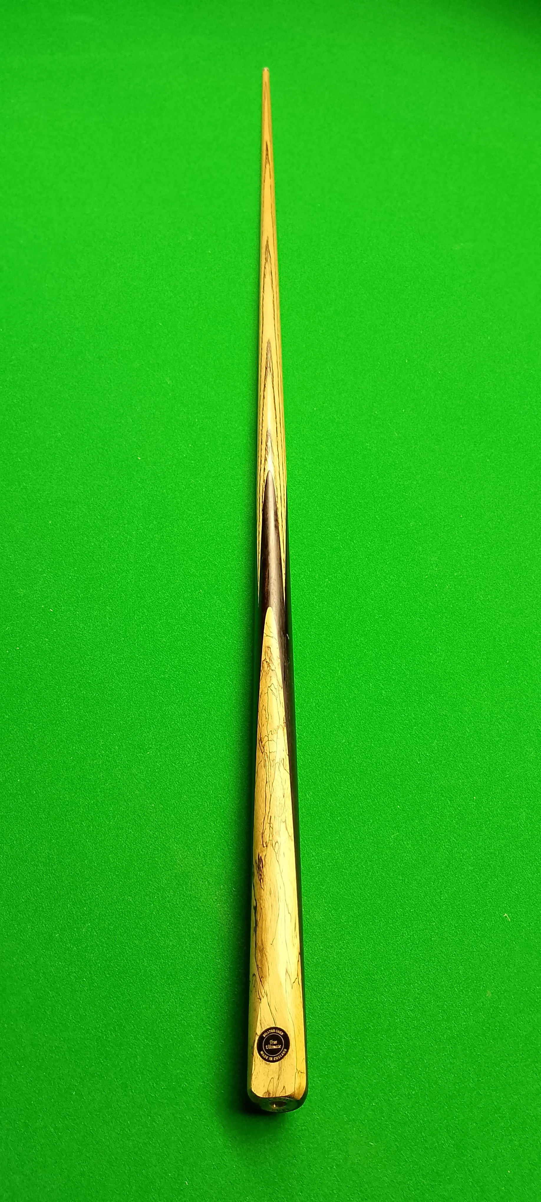 A wooden cue stick for billiards or pool placed on a green felt surface.
