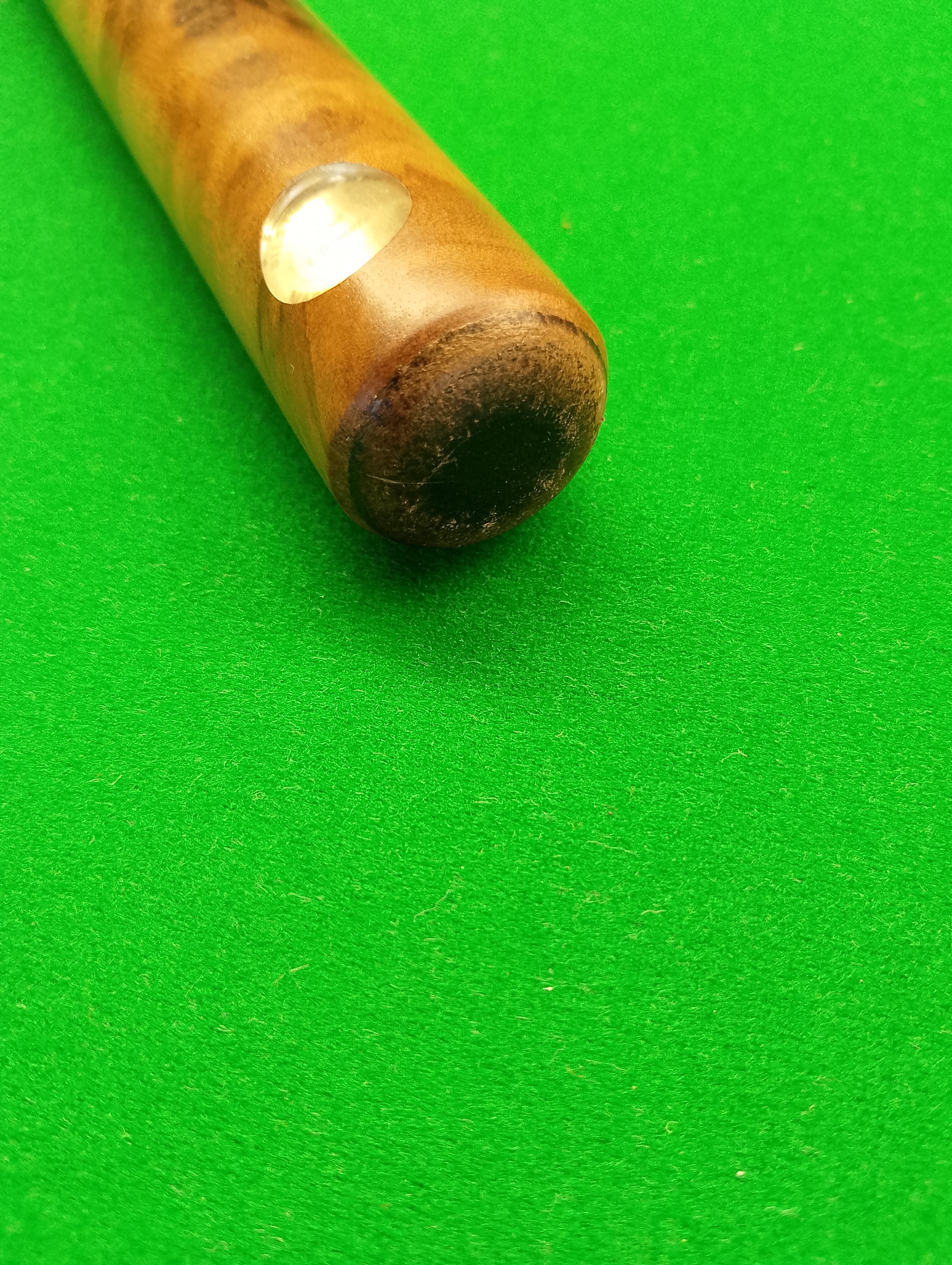 Close-up of a cue stick tip on a green pool table felt.