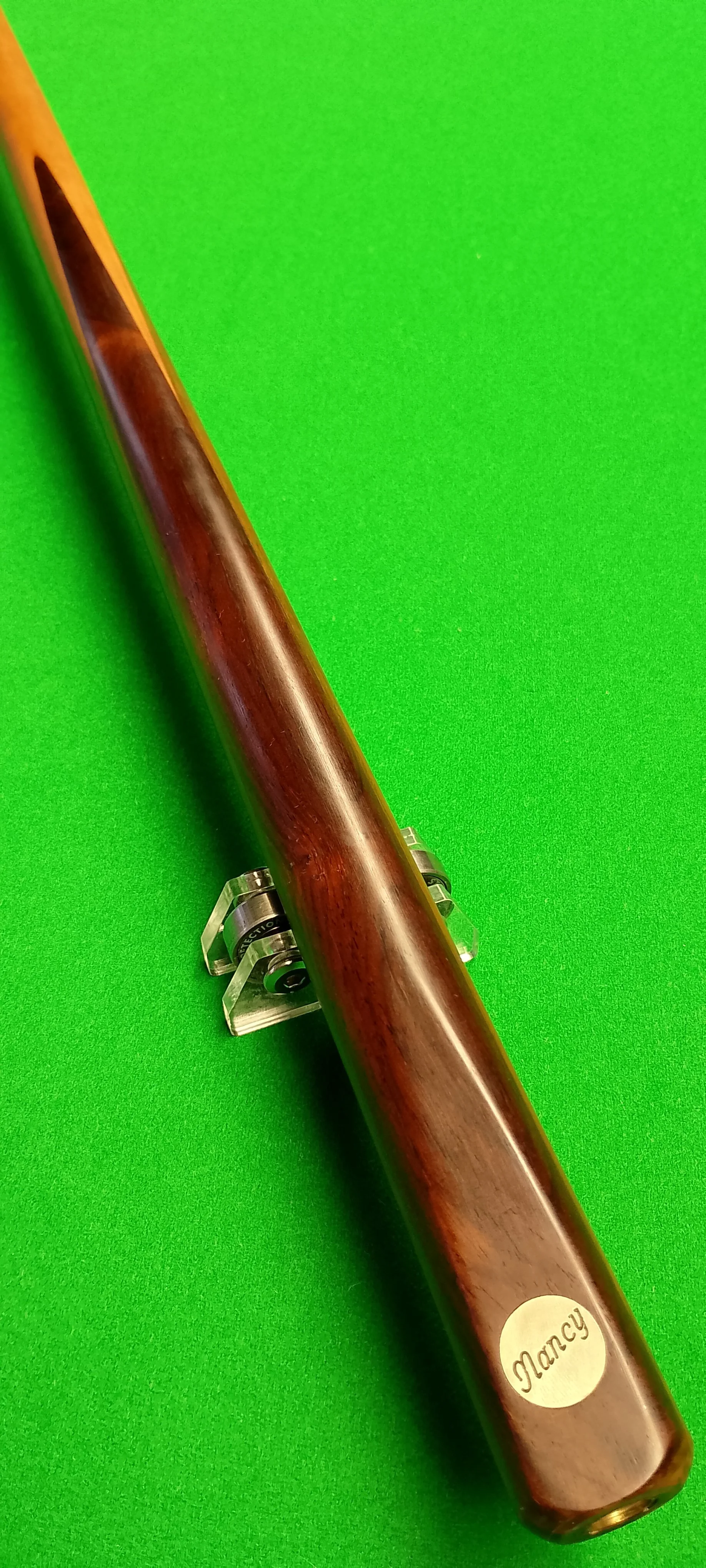 A wooden rifle with a sticker labeled 'Nancy' placed on a green surface.