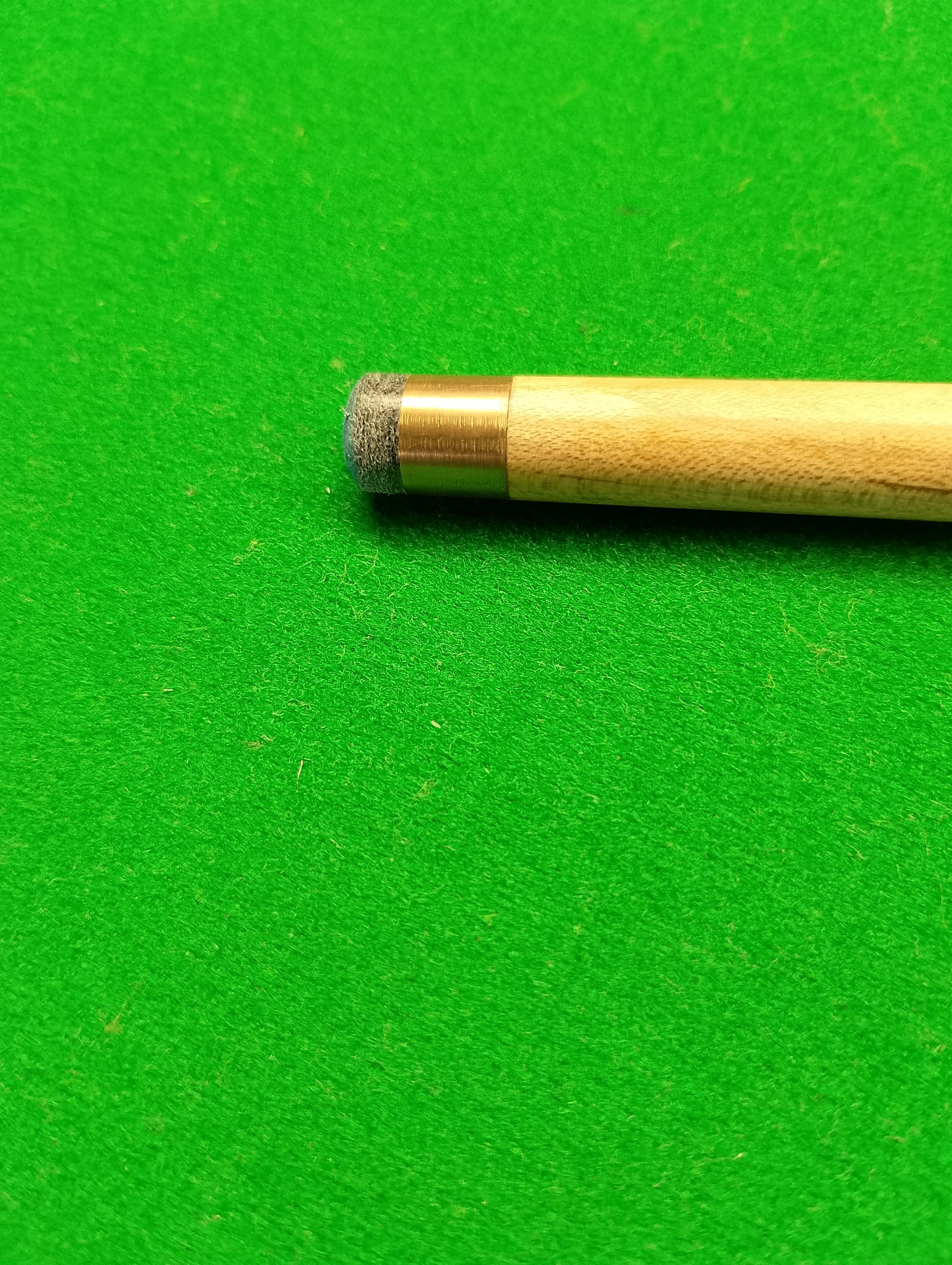 Close-up of a wooden cue stick with a gray felt tip resting on a green felt surface.