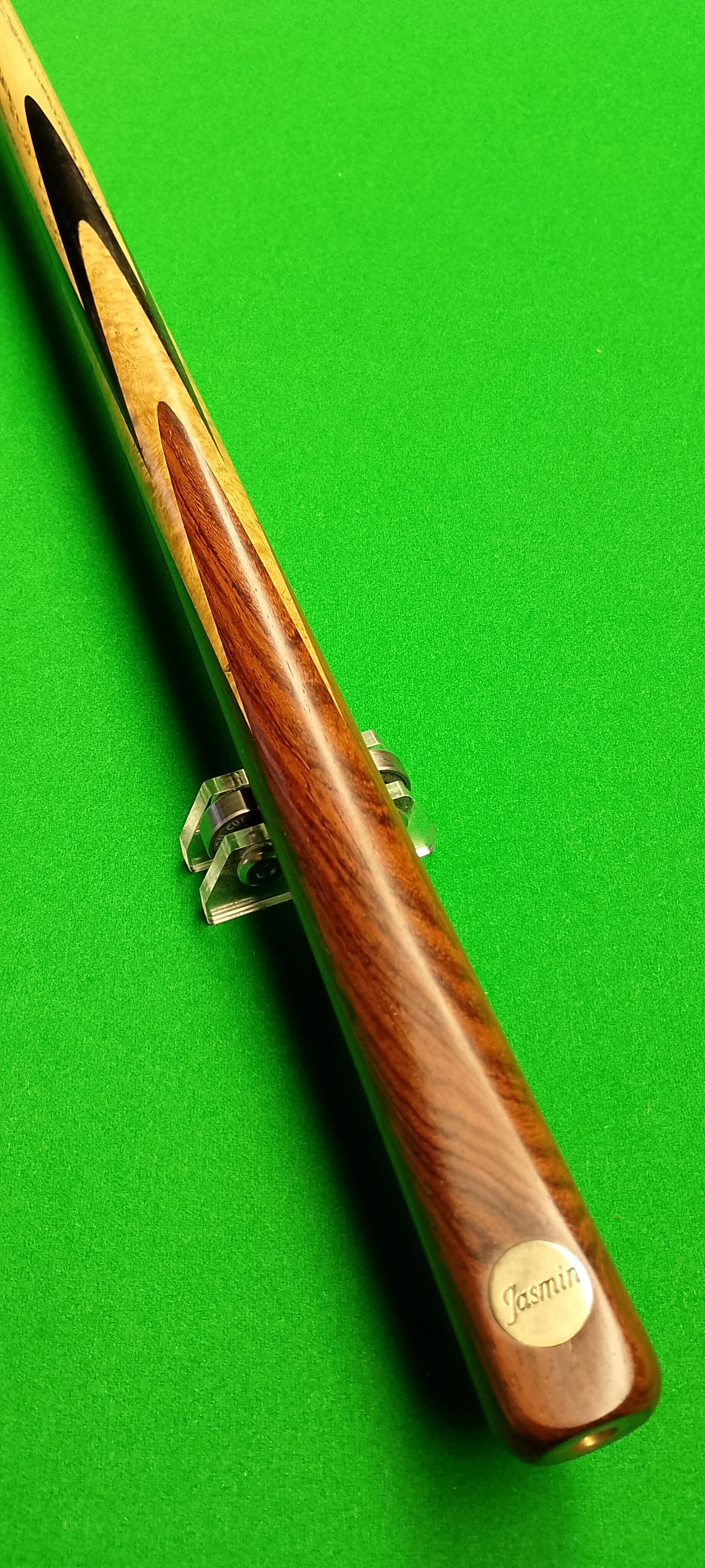 A wooden cue stick with a metal plaque engraved with the name Jasmine, placed on a green surface.