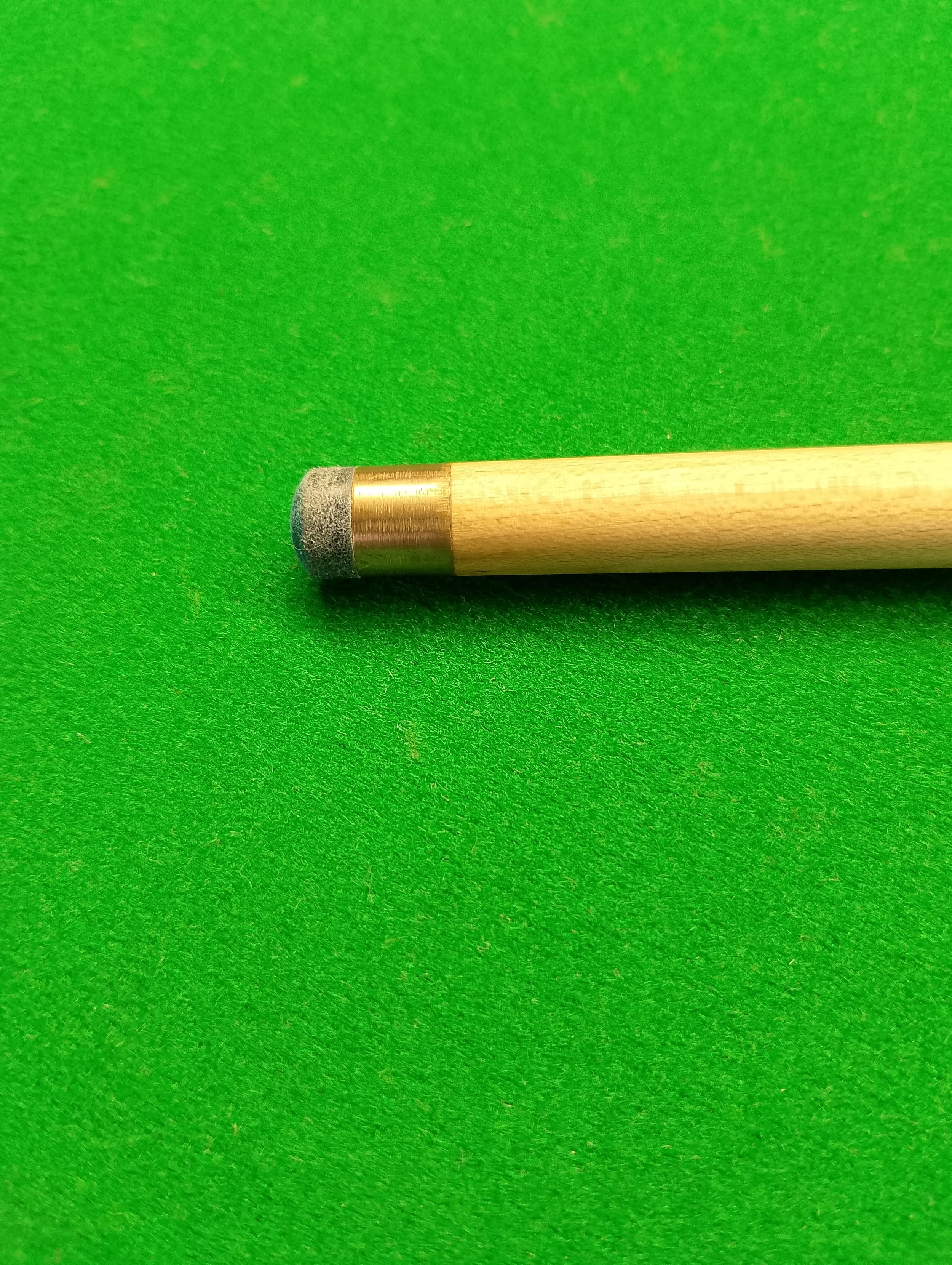 Billiard cue stick lying on green pool table felt with a gray tip.