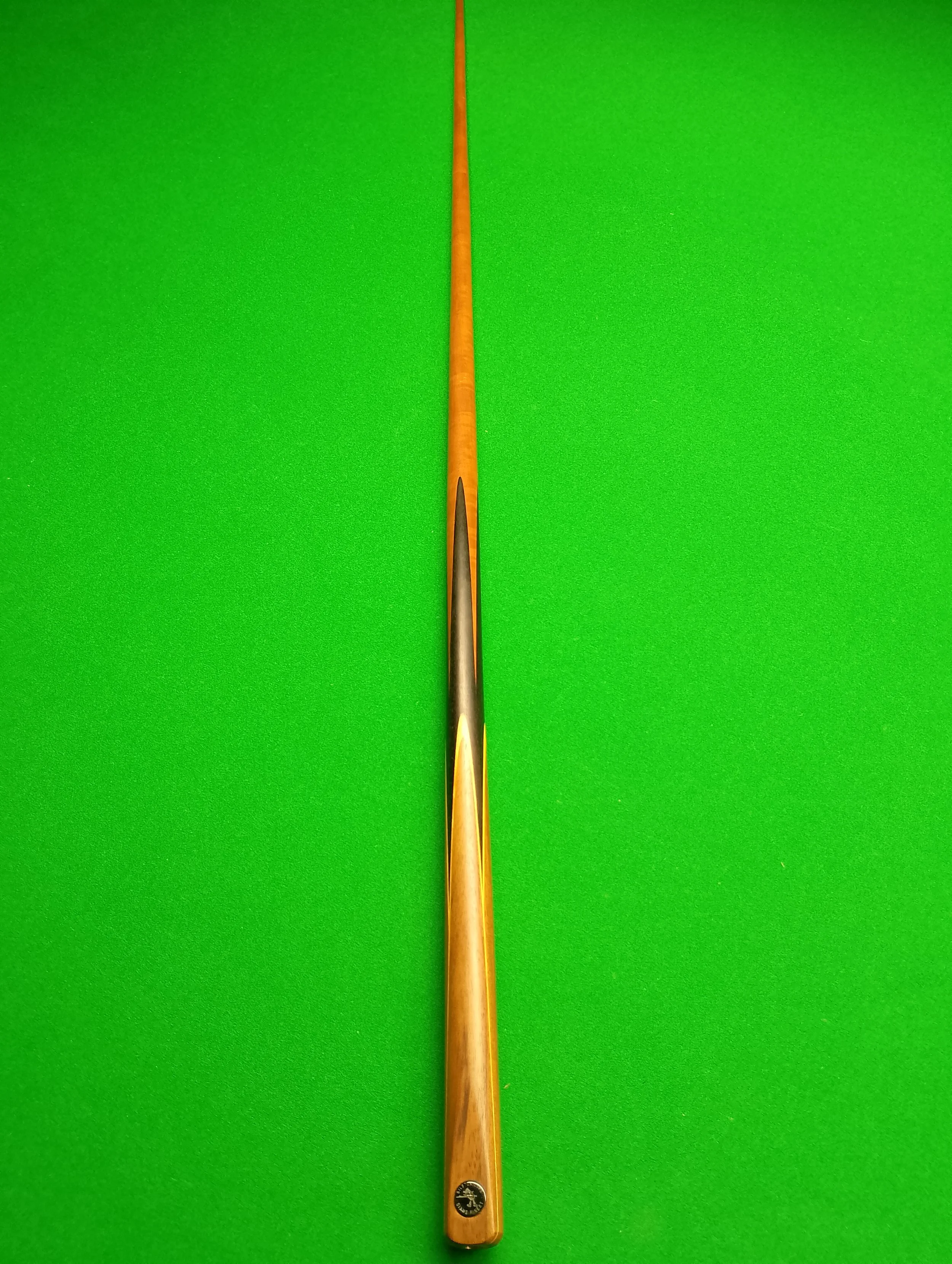 A wooden cue stick positioned vertically on a green pool table.