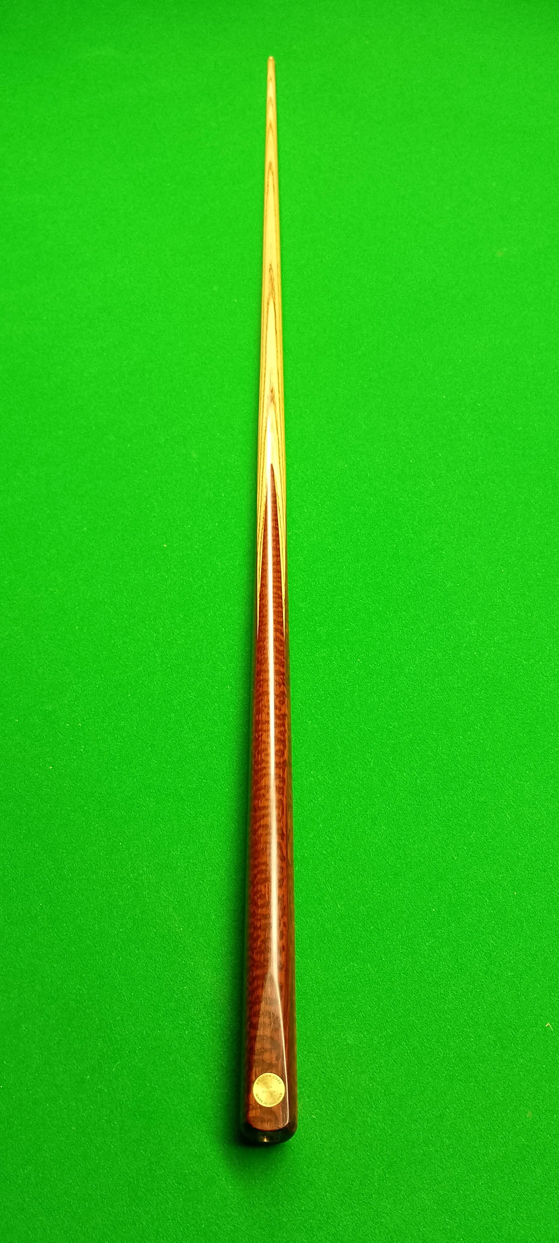 A pool cue stick with a wooden finish placed on a green pool table cloth.
