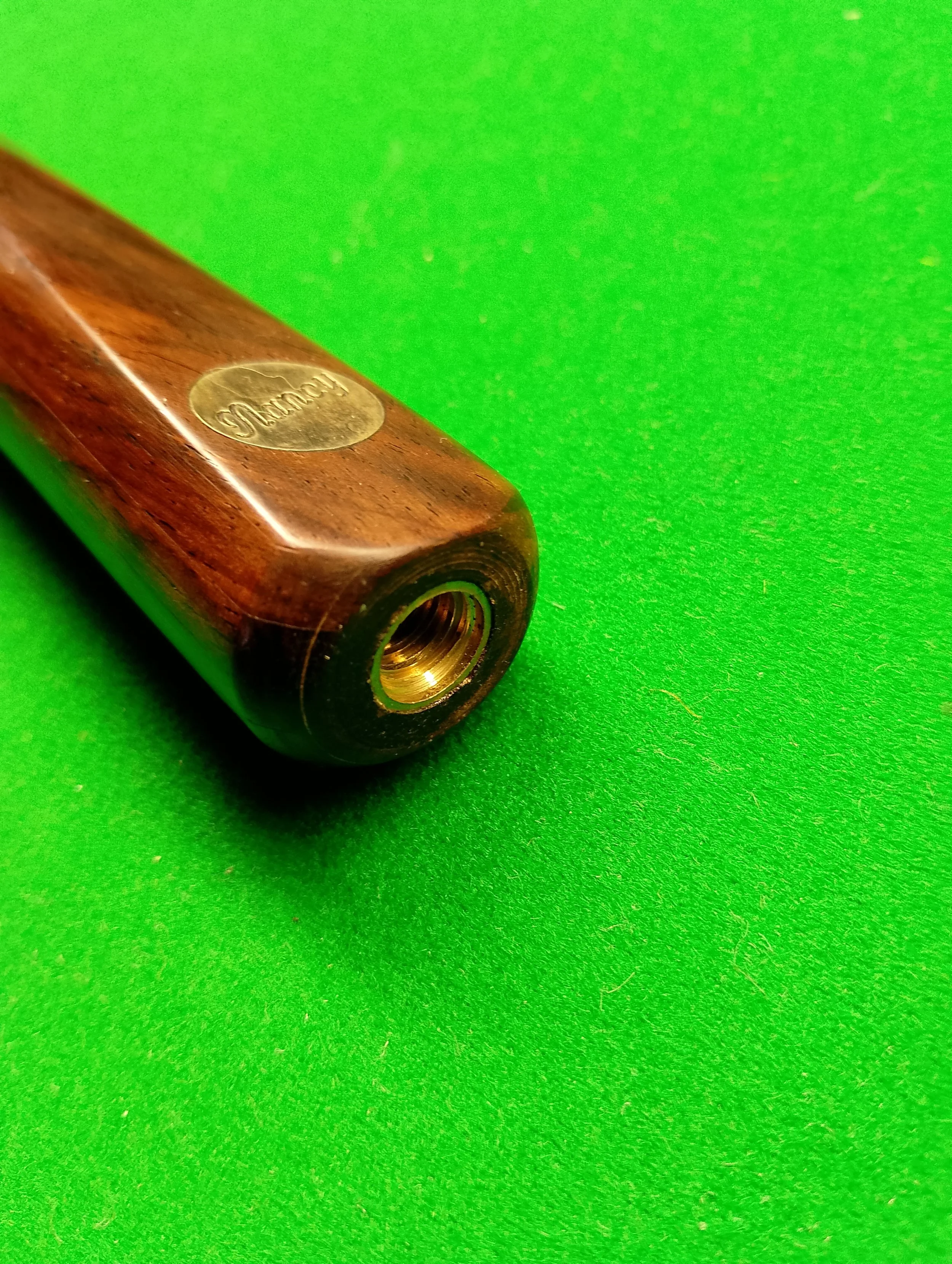 Close-up of a wooden pool cue finger joint with a brass insert on a bright green pool table