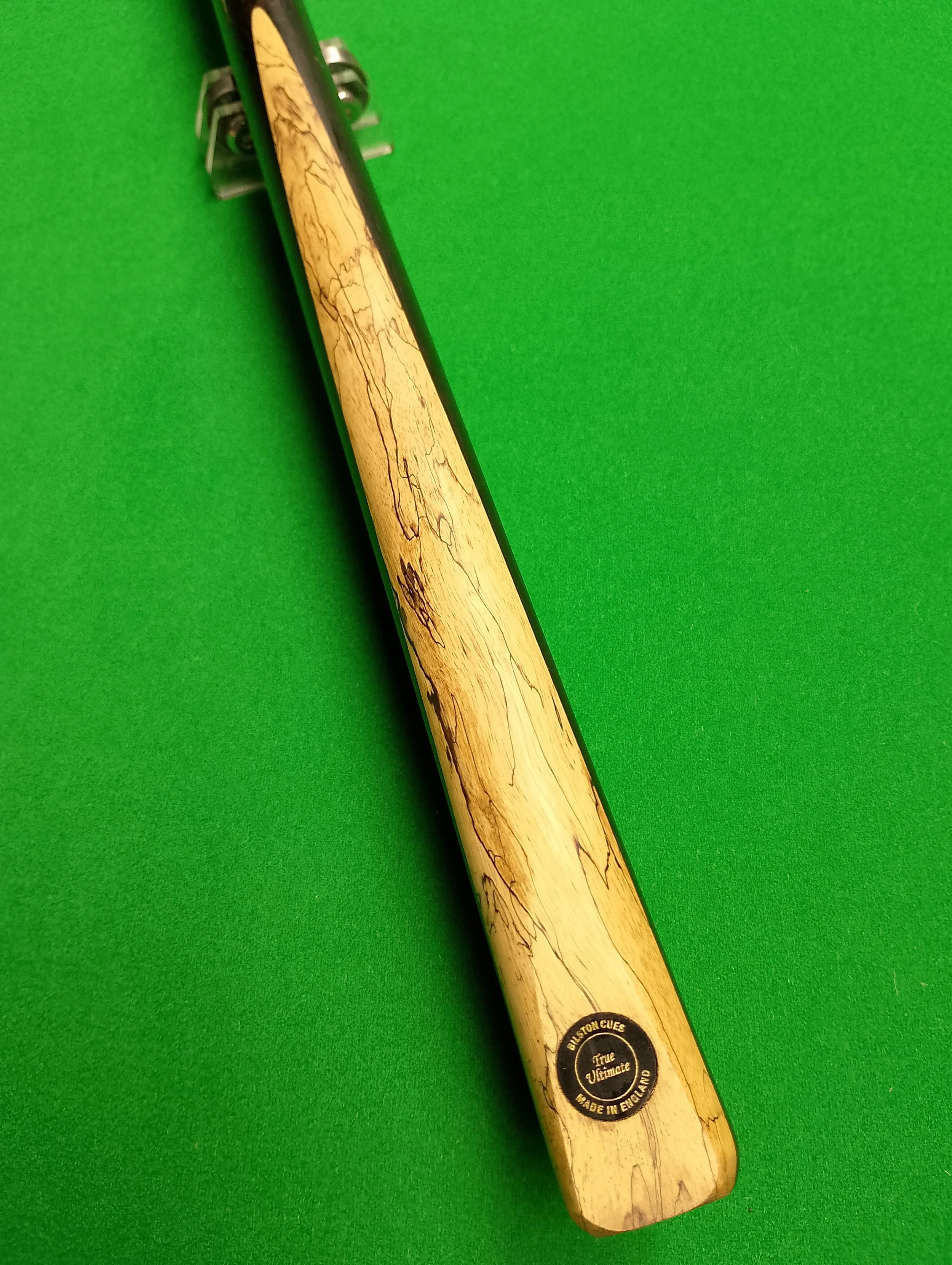 A snooker cue with a light-colored, marbled wood pattern lying on a bright green felt billiard table.