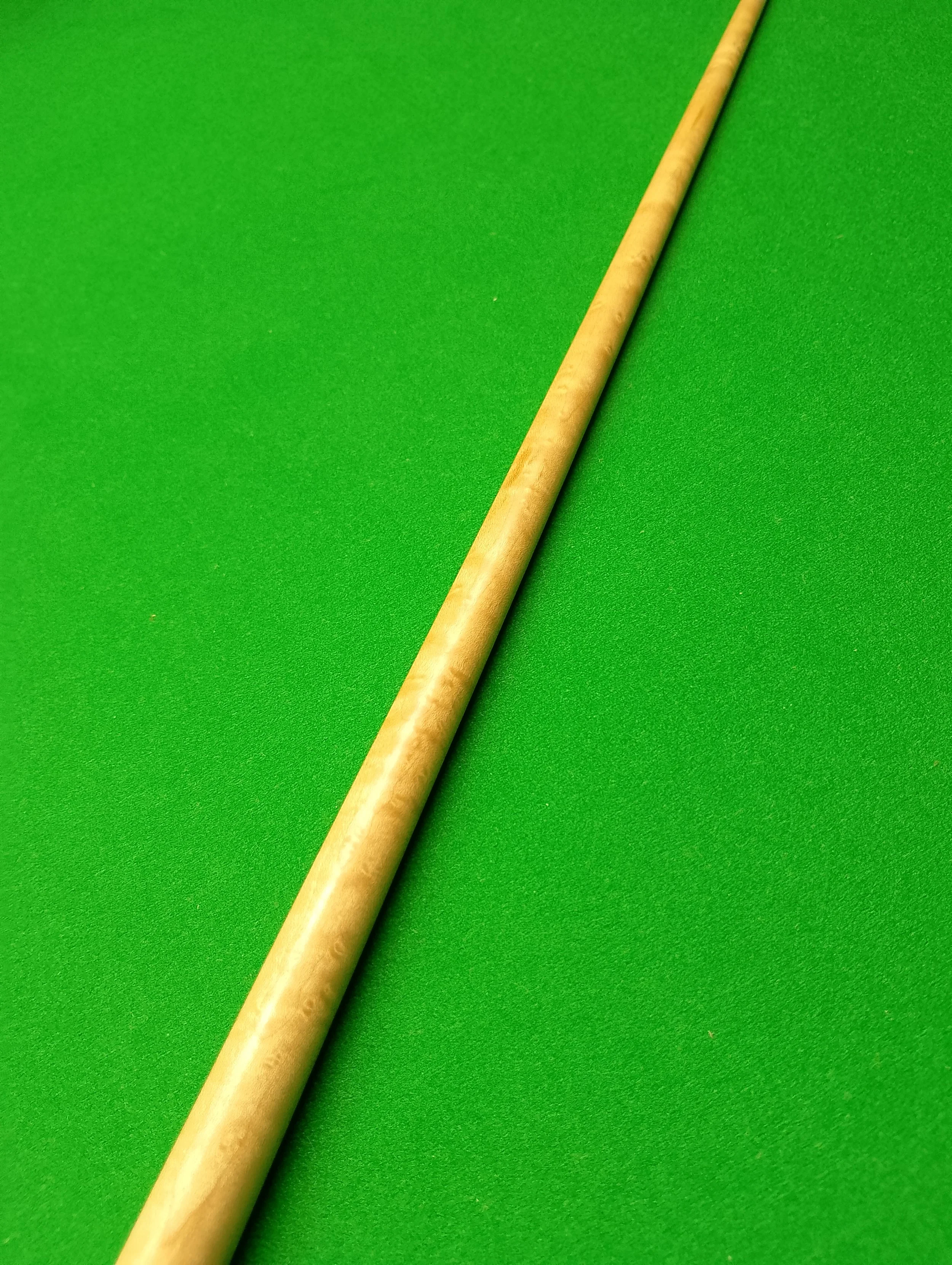 Close-up of a beige pool cue stick resting on a green pool table.