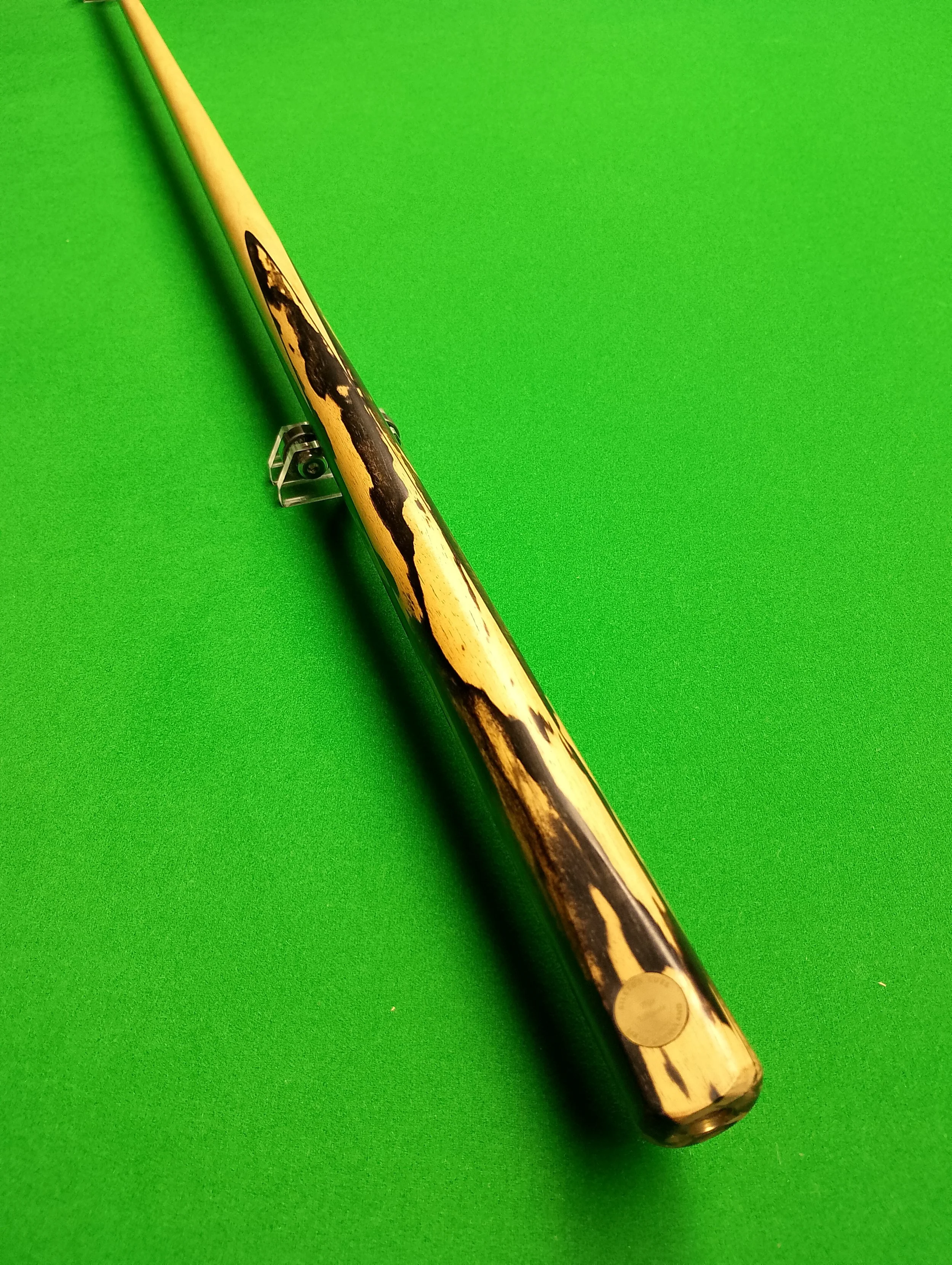 A wooden pool cue with a black and tan patterned design lying on a green pool table.