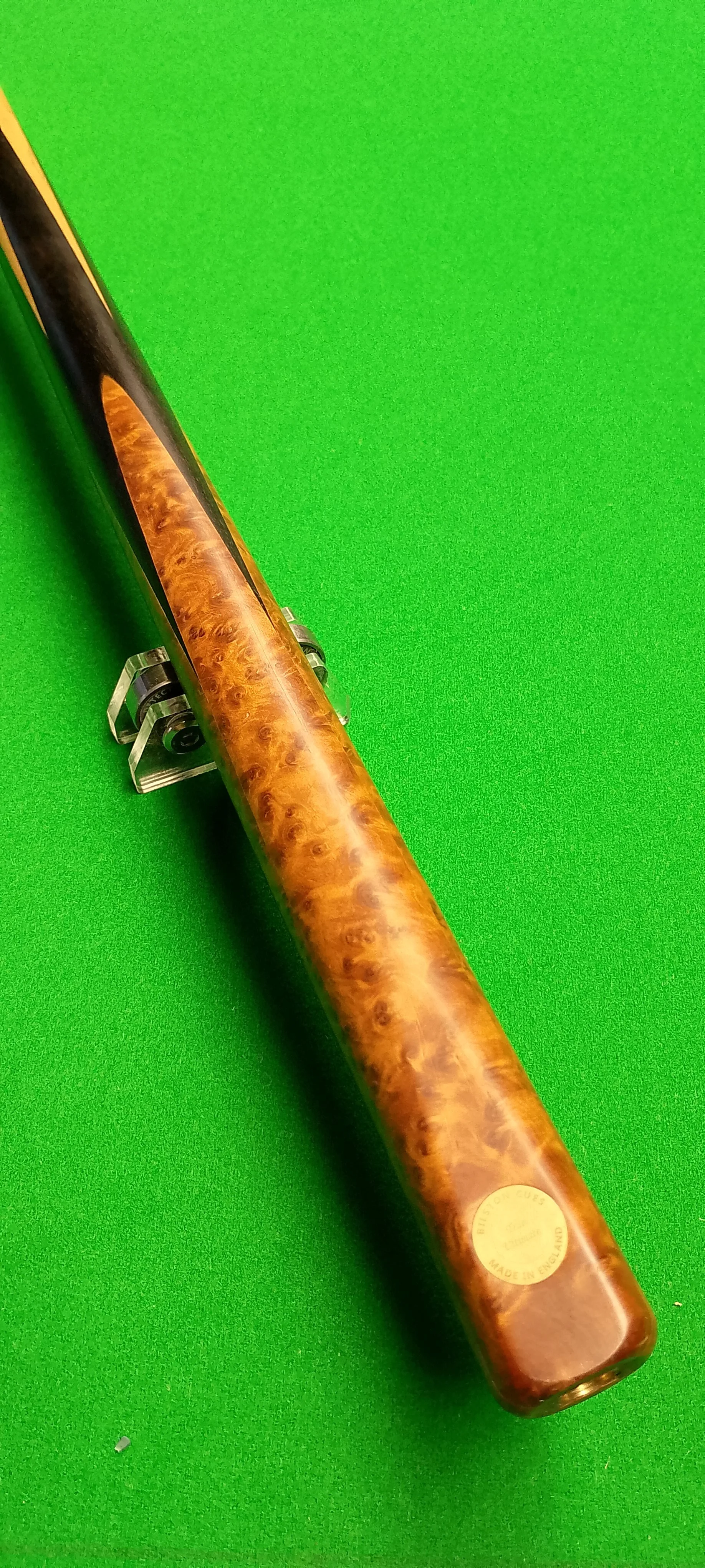 Close-up of a wooden cue stick on a green pool table.