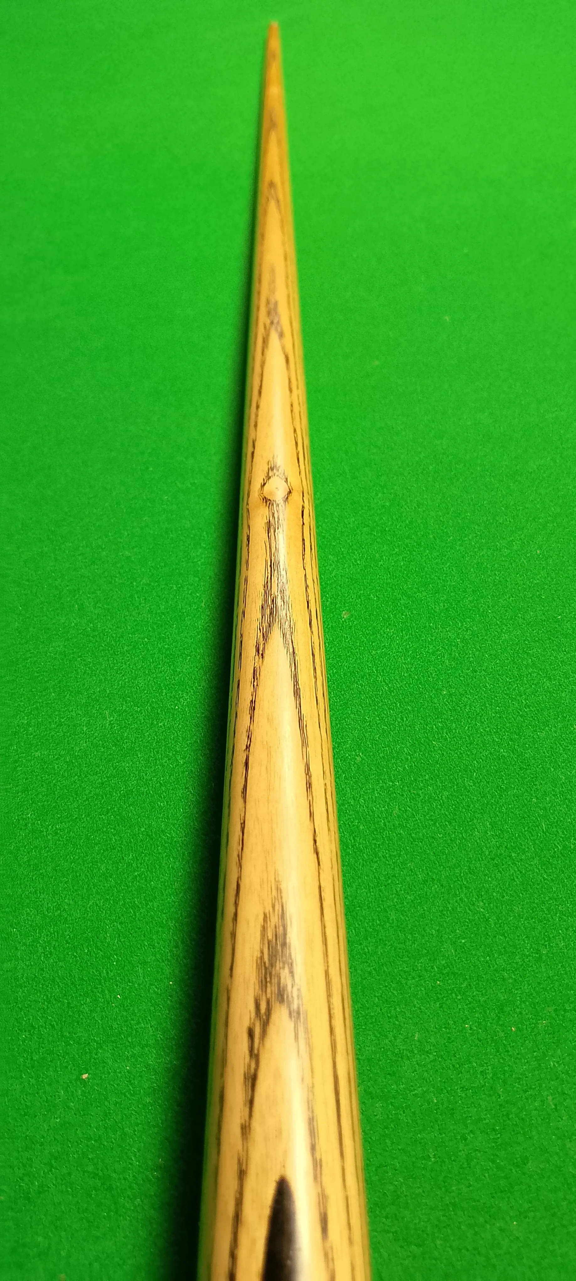 Close-up of a wooden cue stick on a green billiards table.
