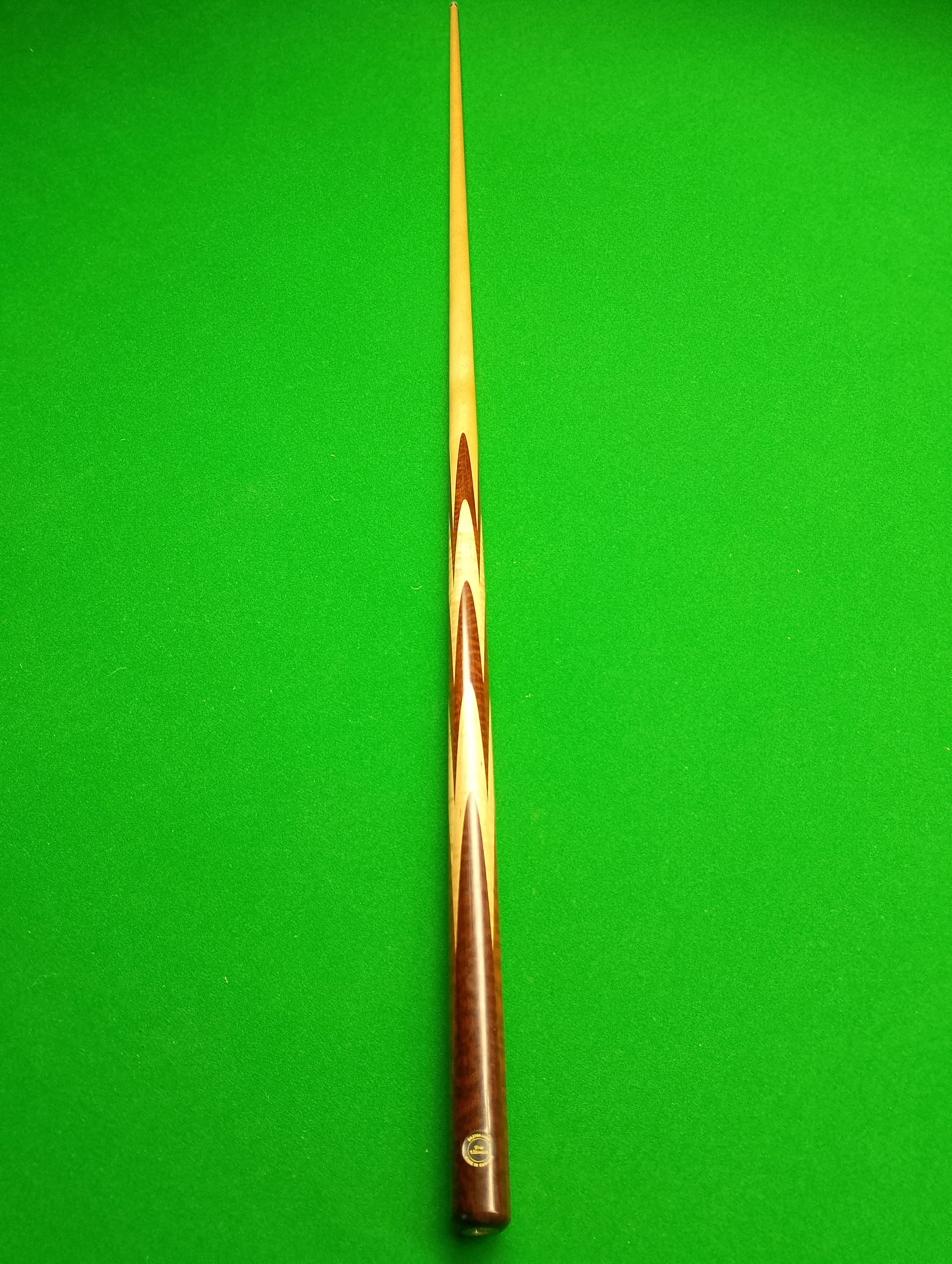 A wooden pool cue with a decorative pattern, placed on a green pool table felt.
