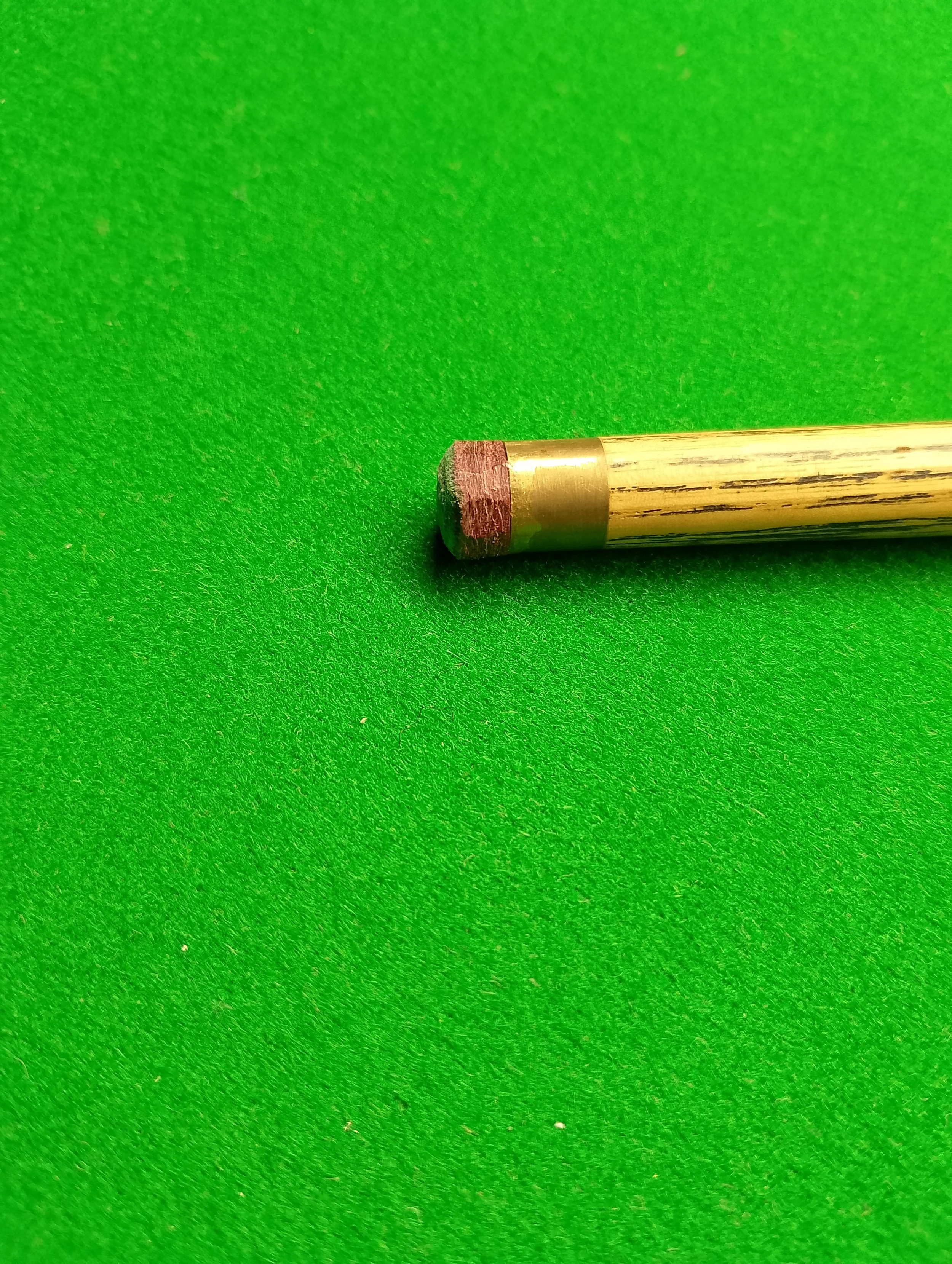 A close-up of a cue tip and a portion of a wooden cue stick on a green felt billiard table.