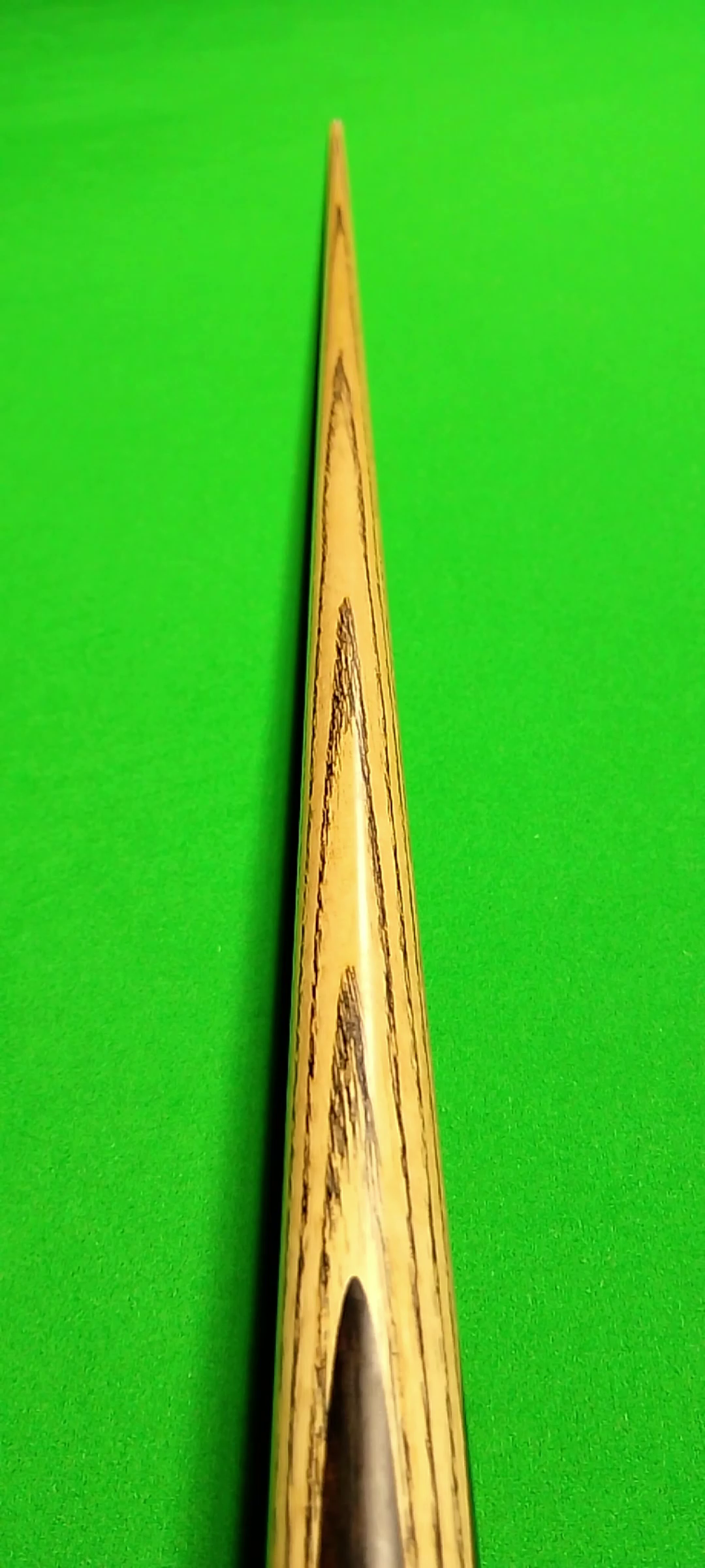 Close-up of a wooden cue stick on a green pool table.