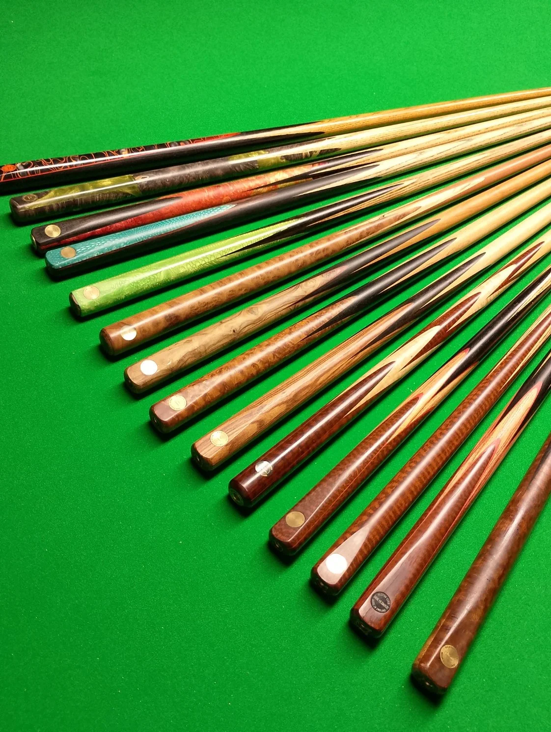 A set of billiard cue sticks arranged diagonally on a green pool table.