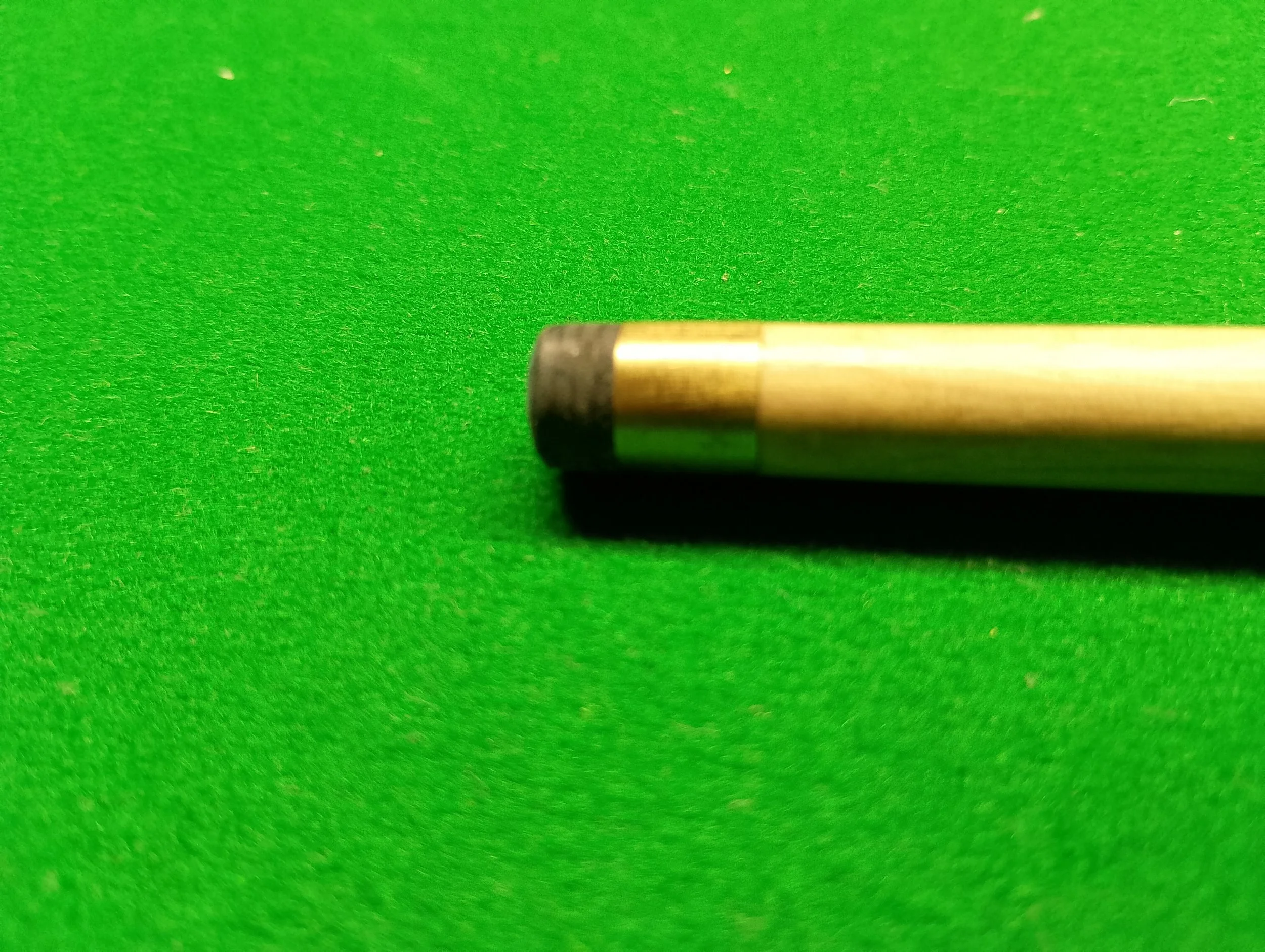 Close-up of a pool cue on a green felt pool table.