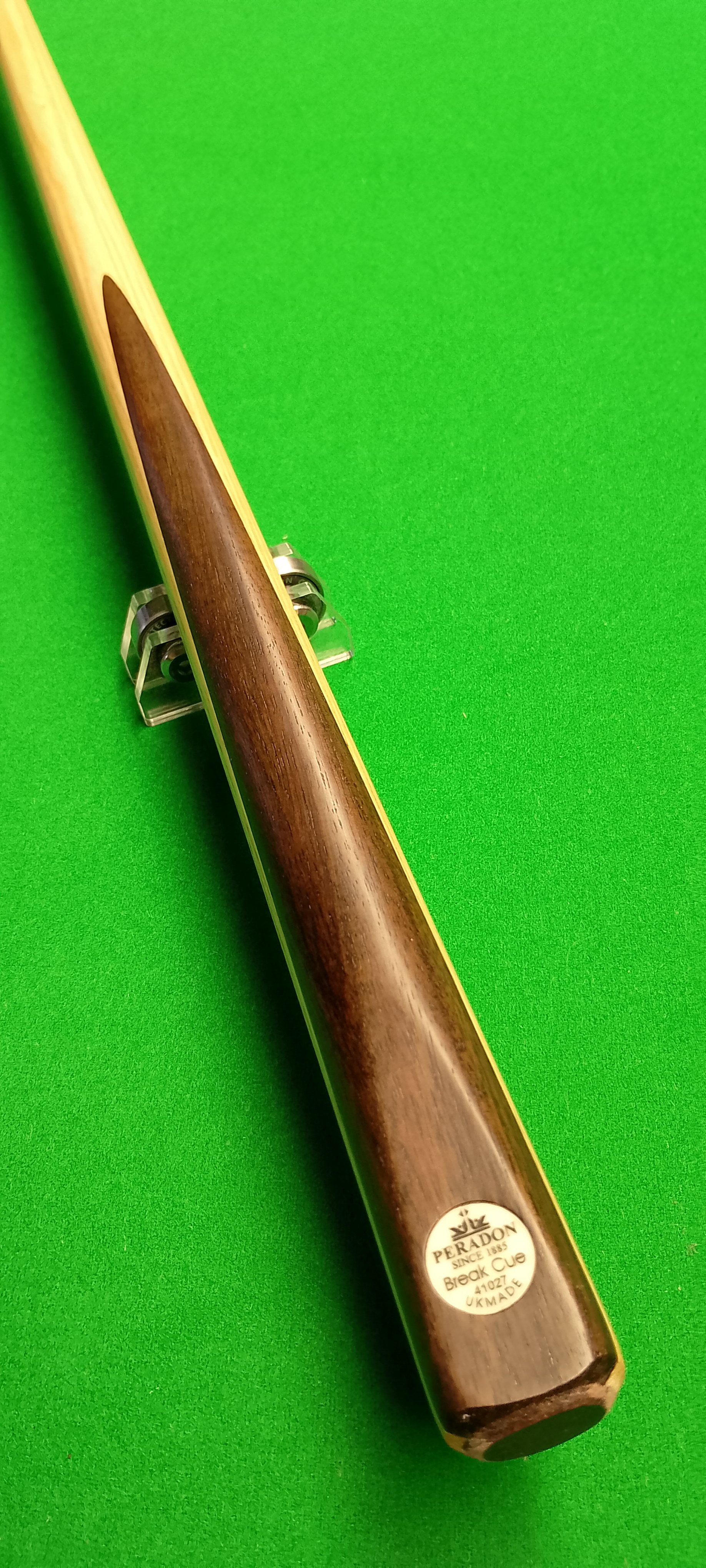 A snooker cue resting on a cue stand on a green snooker table.