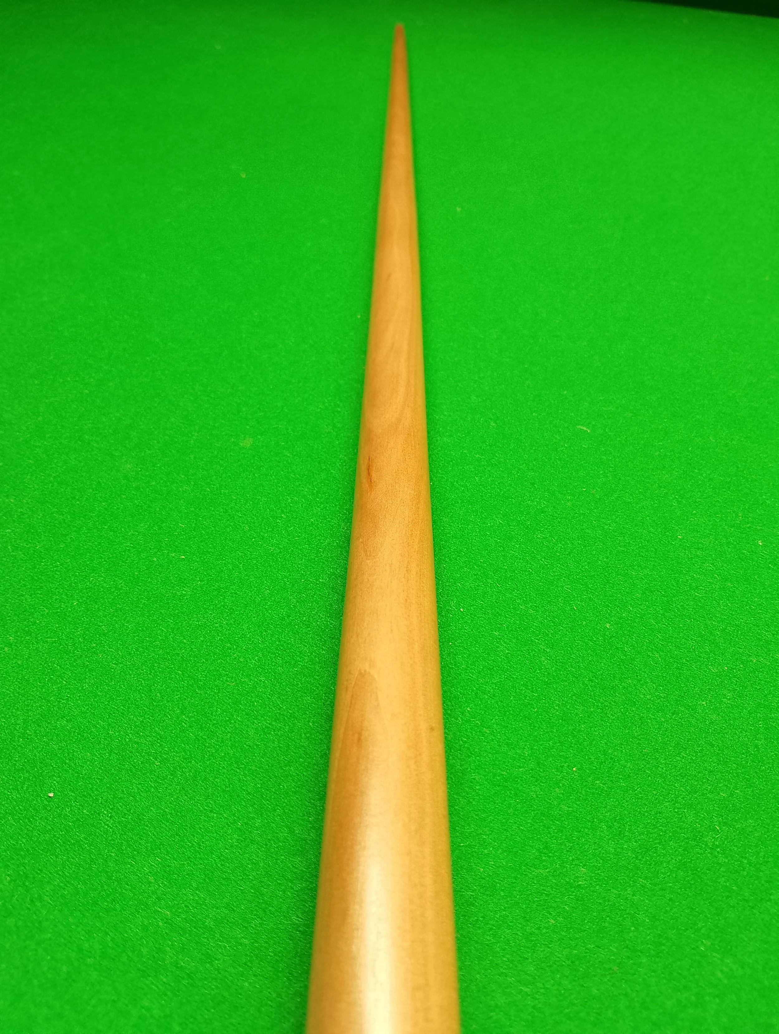 A wooden cue stick resting on a green felt snooker or billiards table.