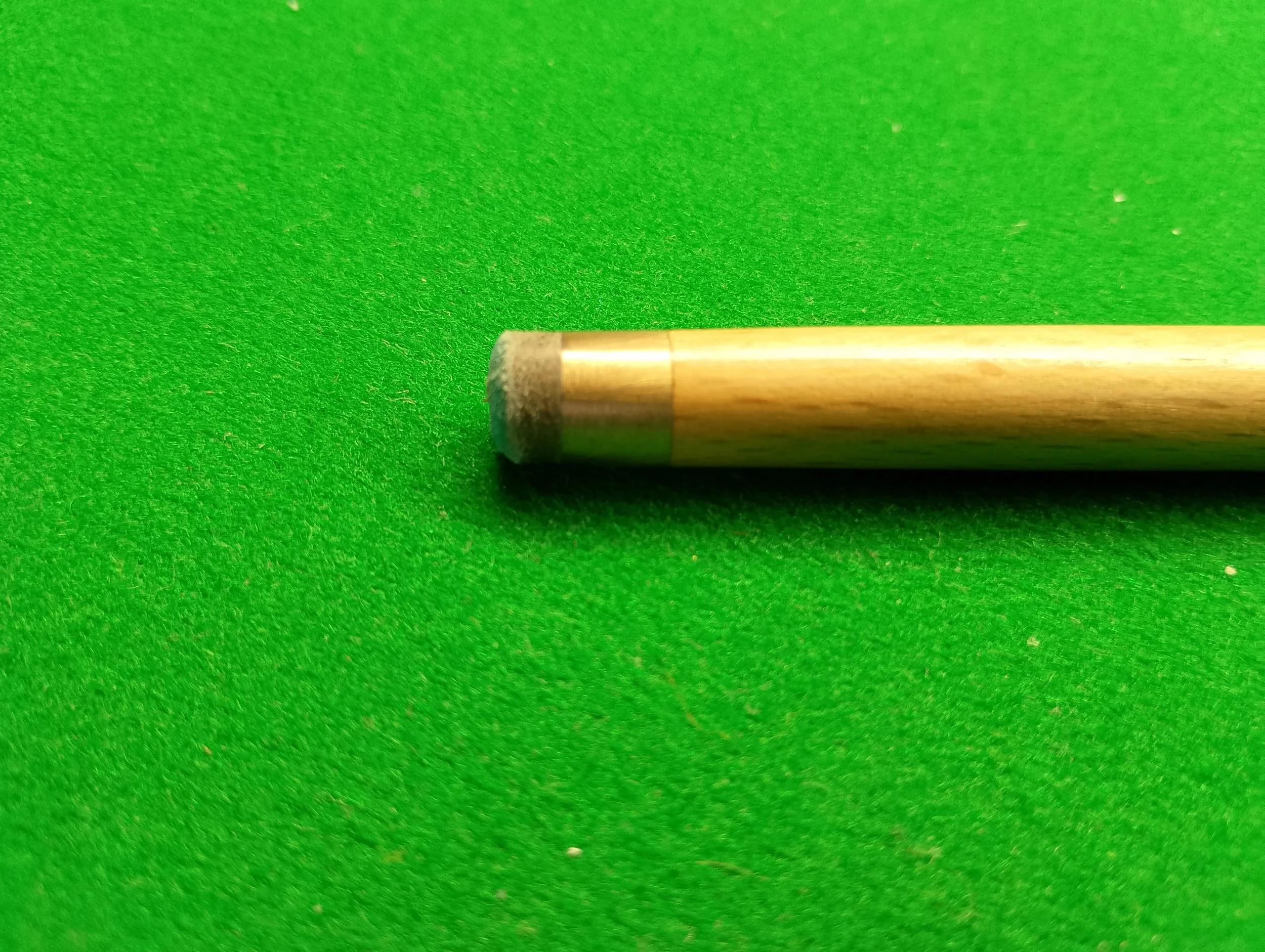 Close-up of a billiard cue stick on a green felt surface.