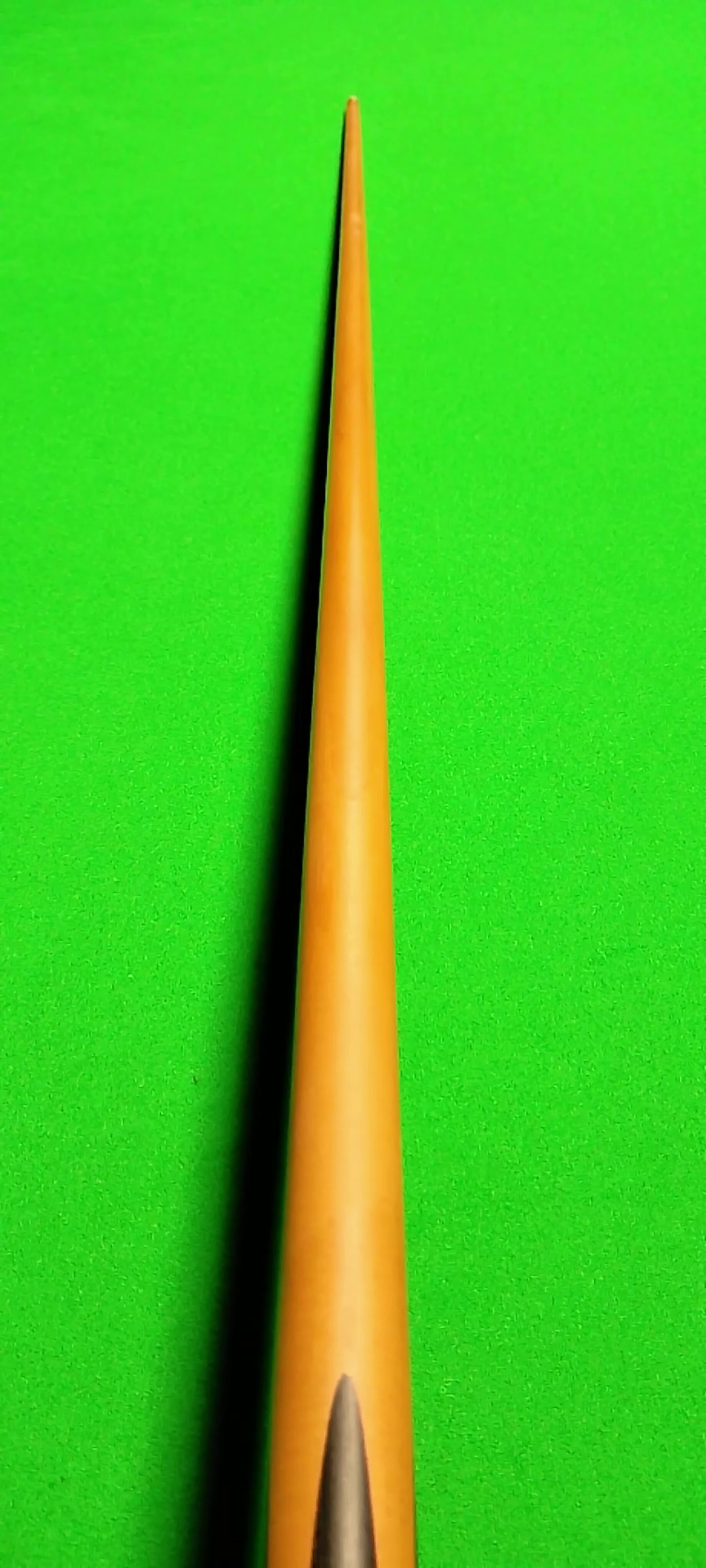 Close-up of a yellow dart with a metal tip on a bright green background.
