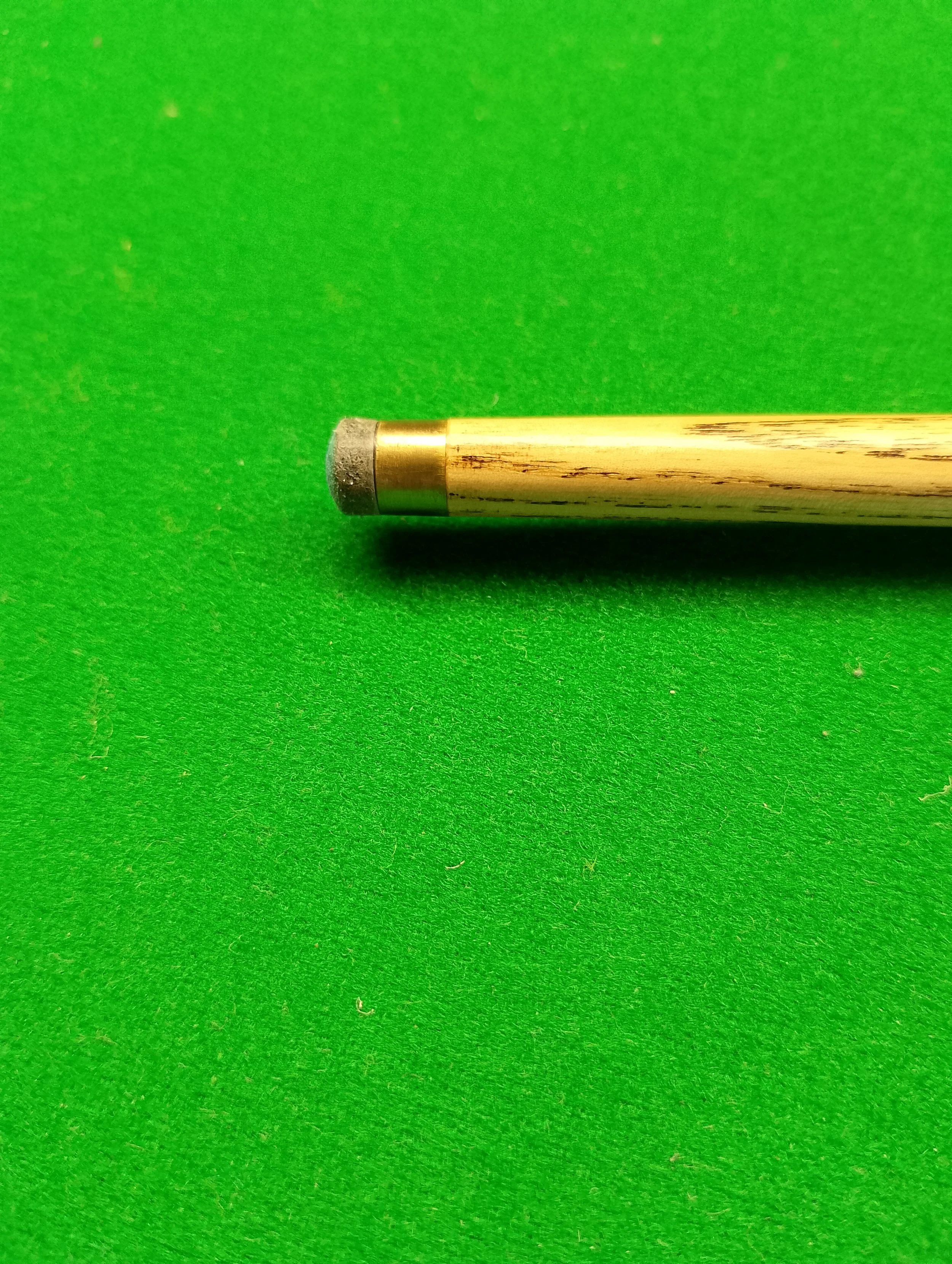 A close-up of a brass cue stick with a black rubber tip on a green felt billiard table.