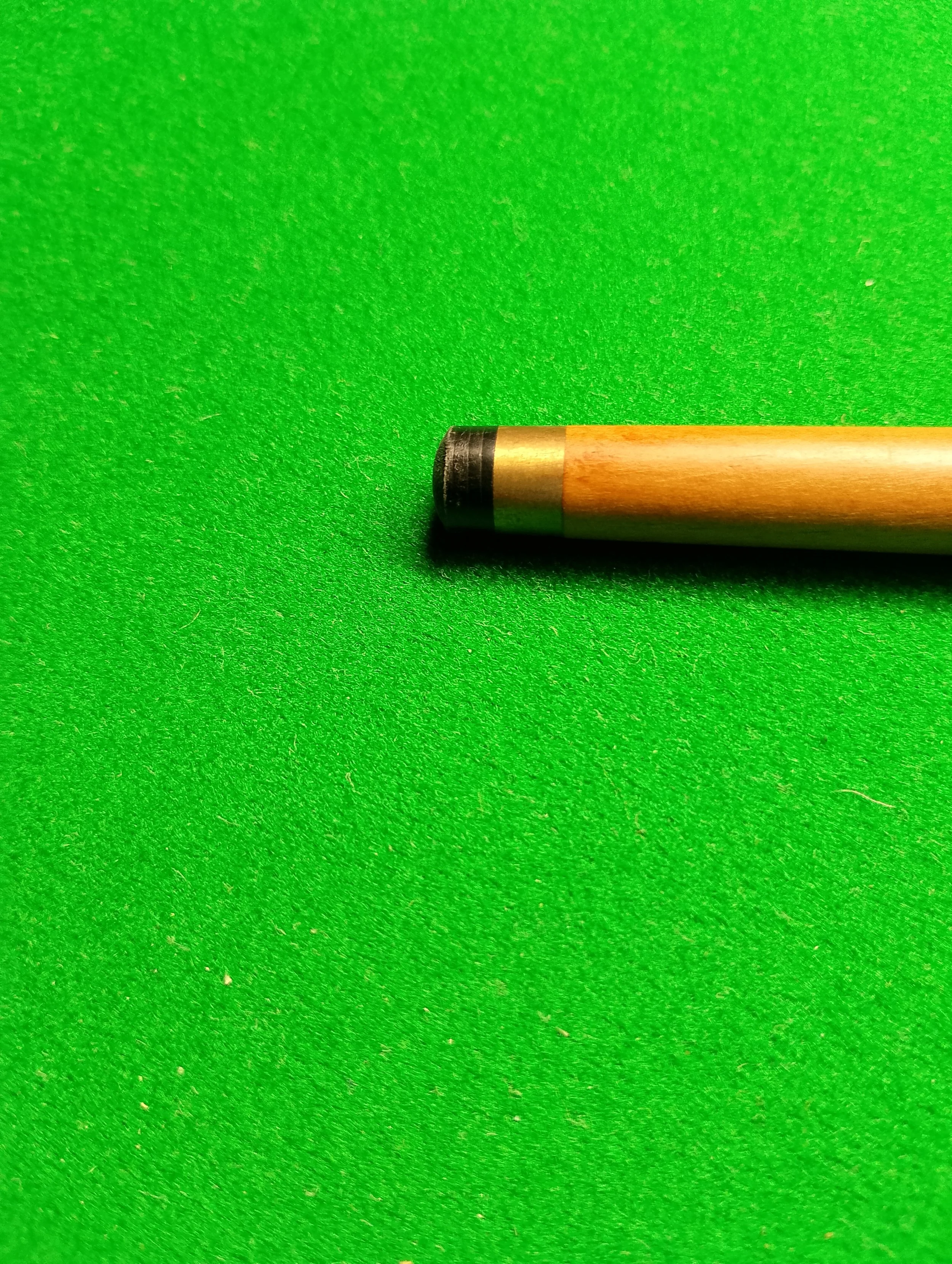 Close-up of a pool cue on a green felt pool table.