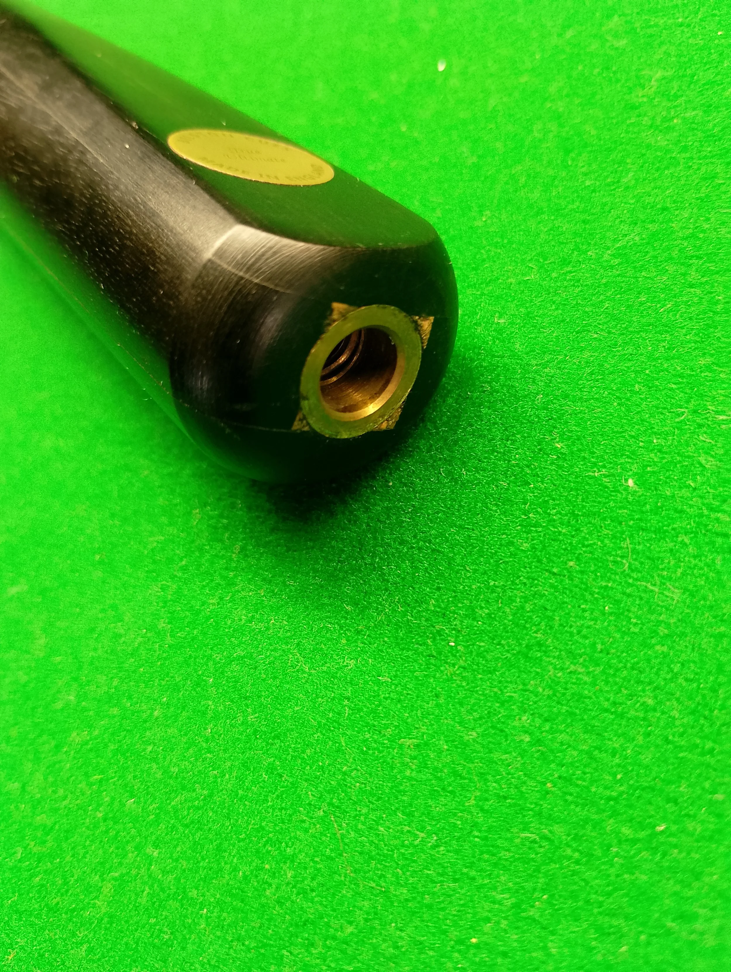 Close-up of a black object with a gold-colored circular opening, placed on a bright green textured surface.